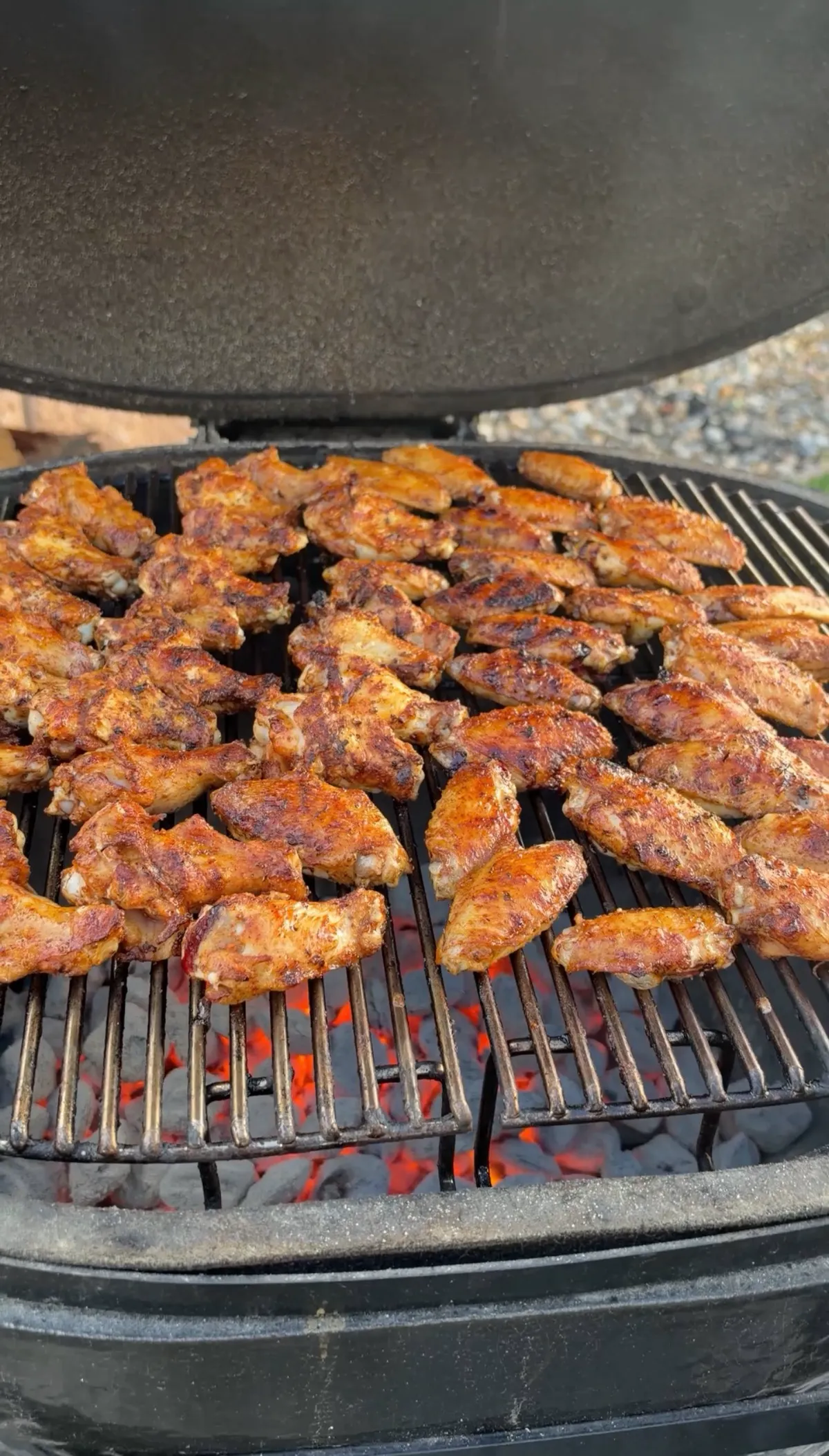 Seasoned chicken wings grilling over glowing charcoal at 300–350°F, skin crisping and charring on cast iron grates