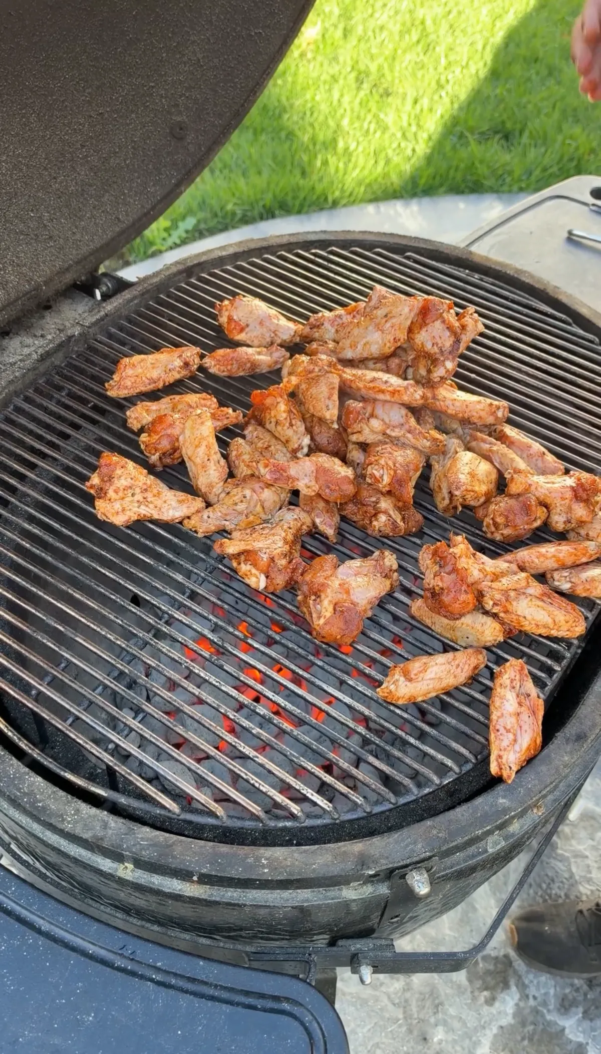 Chicken wings seasoned with poultry seasoning grilling over glowing charcoal on a round kamado-style grill