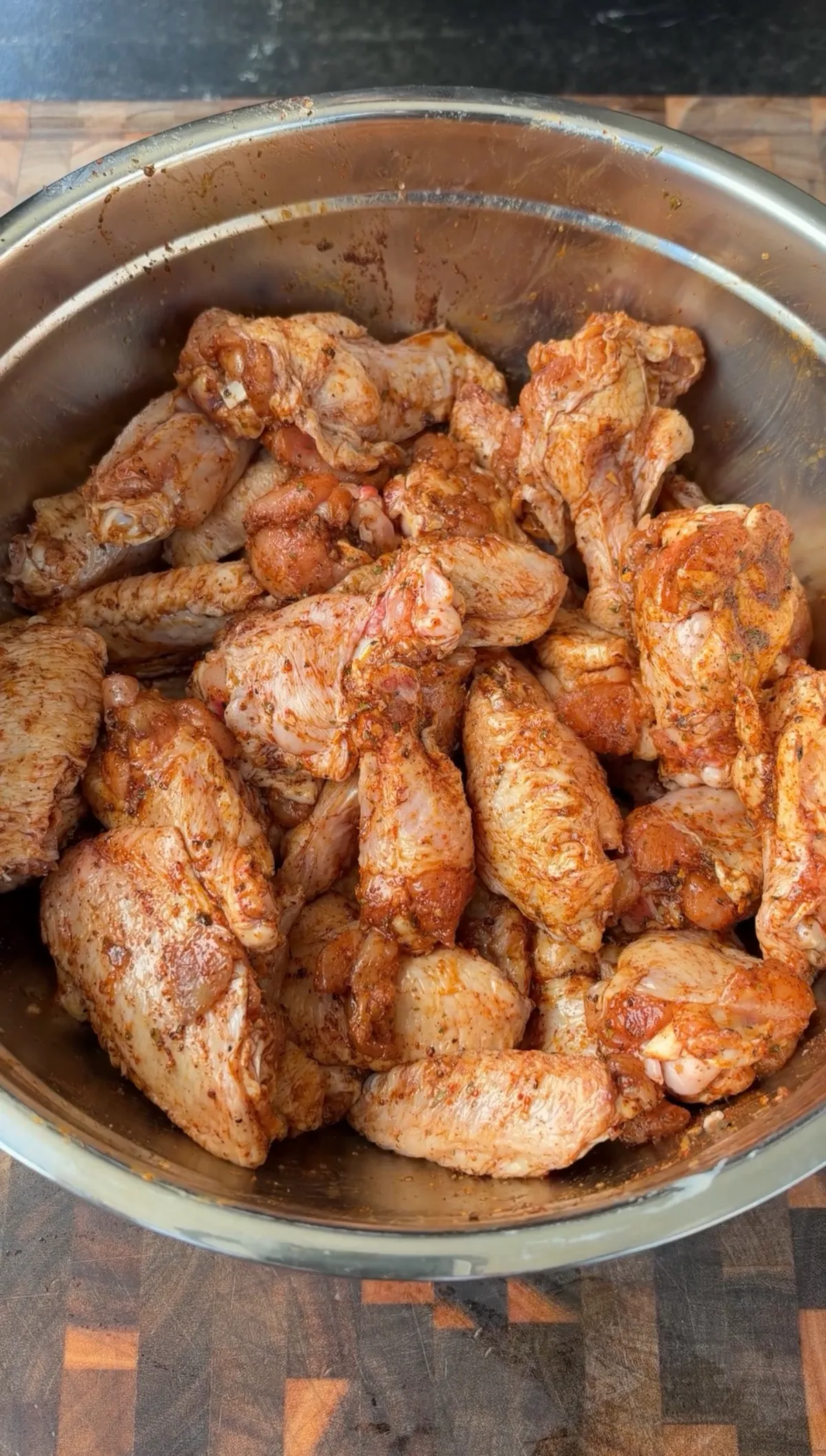 Raw chicken wings coated in poultry seasoning and olive oil, tossed in a stainless steel mixing bowl