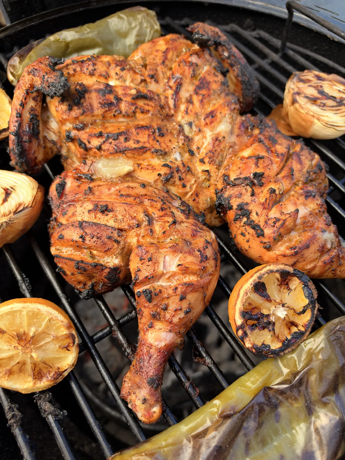 Spatchcocked chicken with chipotle and smoked paprika marinade grilling at 350°F with charred lemon halves and onion