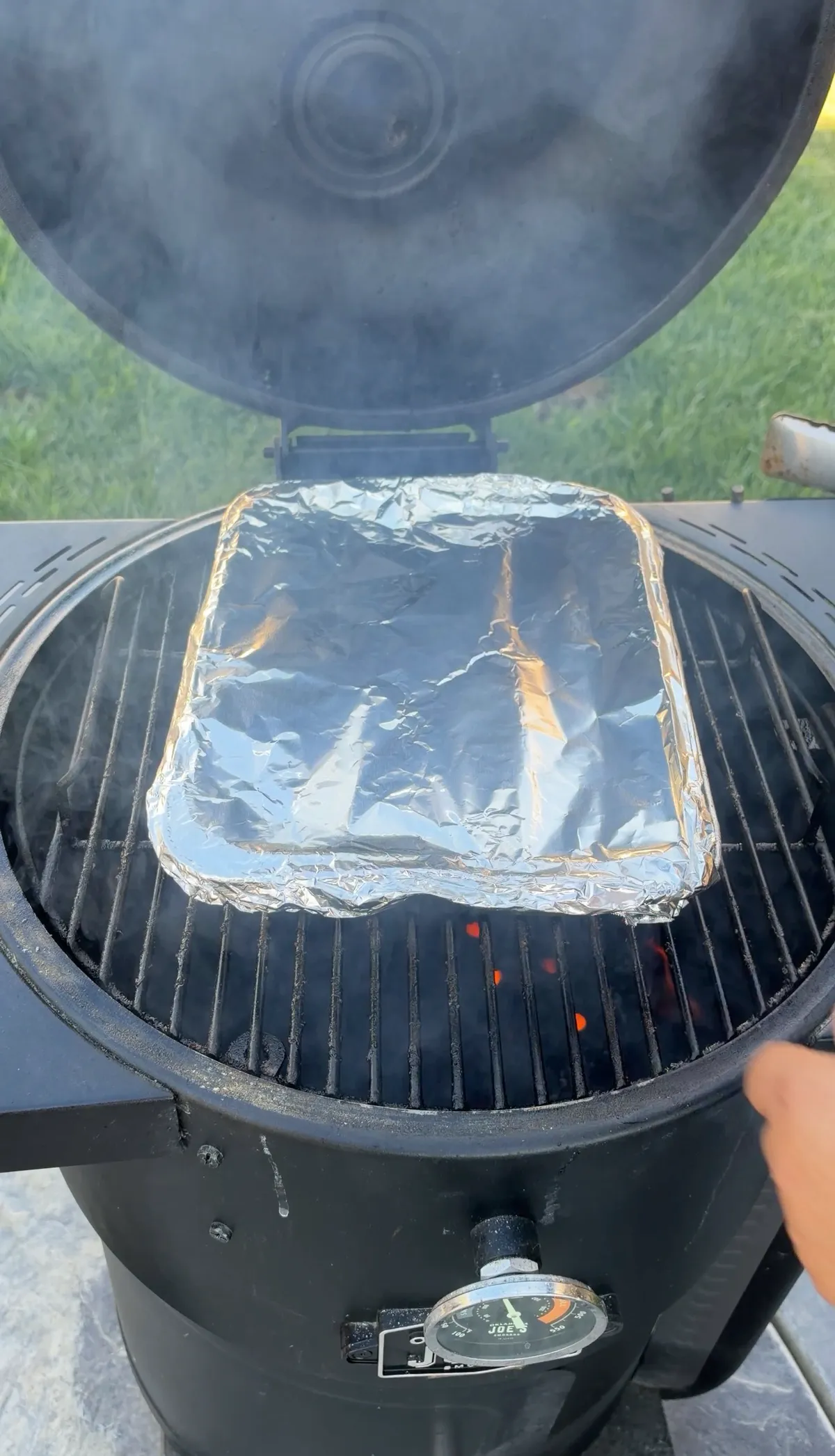 Foil pan of honey BBQ chuck roast burnt ends covered tightly with aluminum foil braising on a charcoal smoker at 250°F