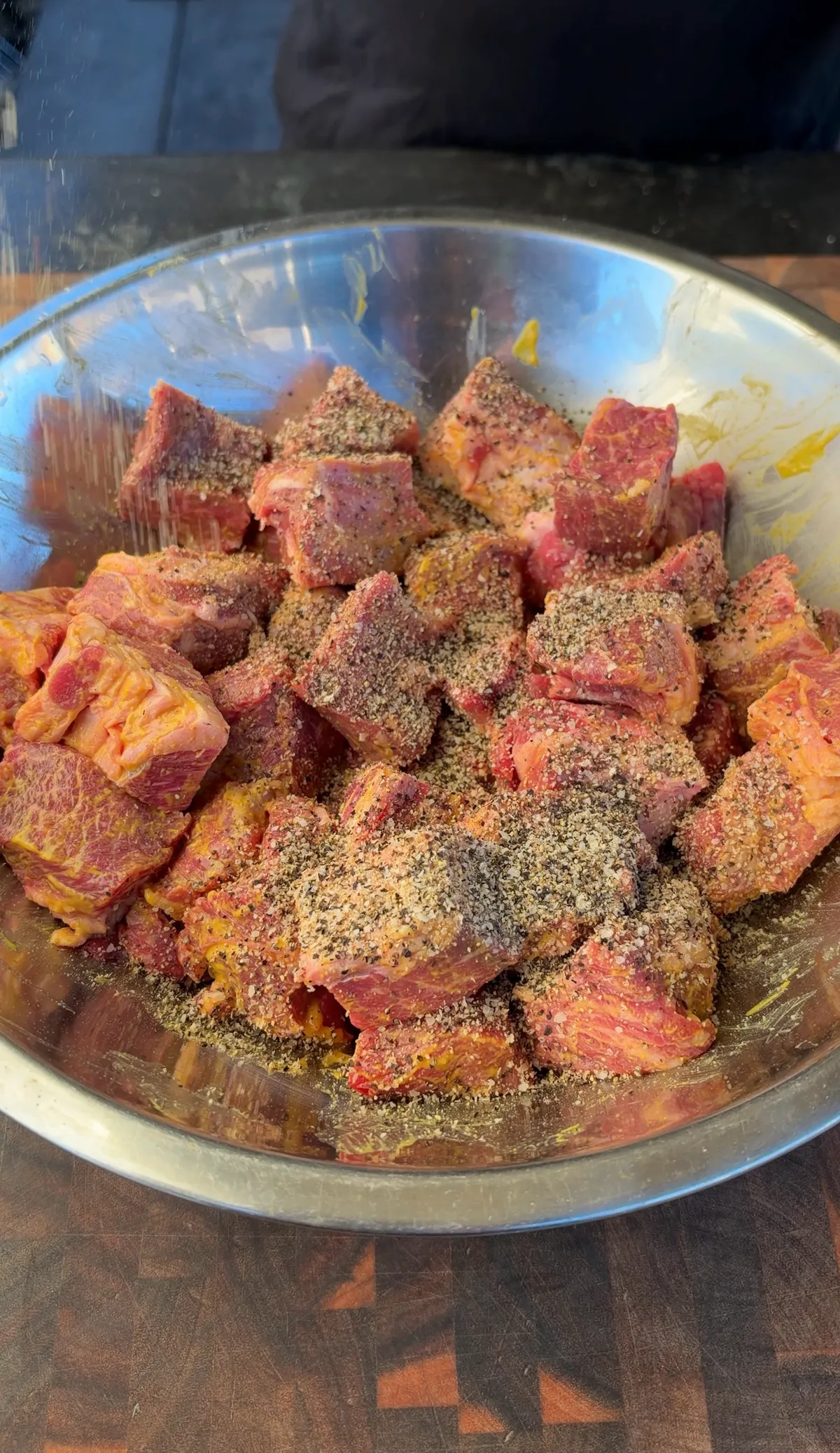 Chuck roast cubes coated in yellow mustard and seasoned with salt, black pepper, and garlic powder in a stainless steel bowl