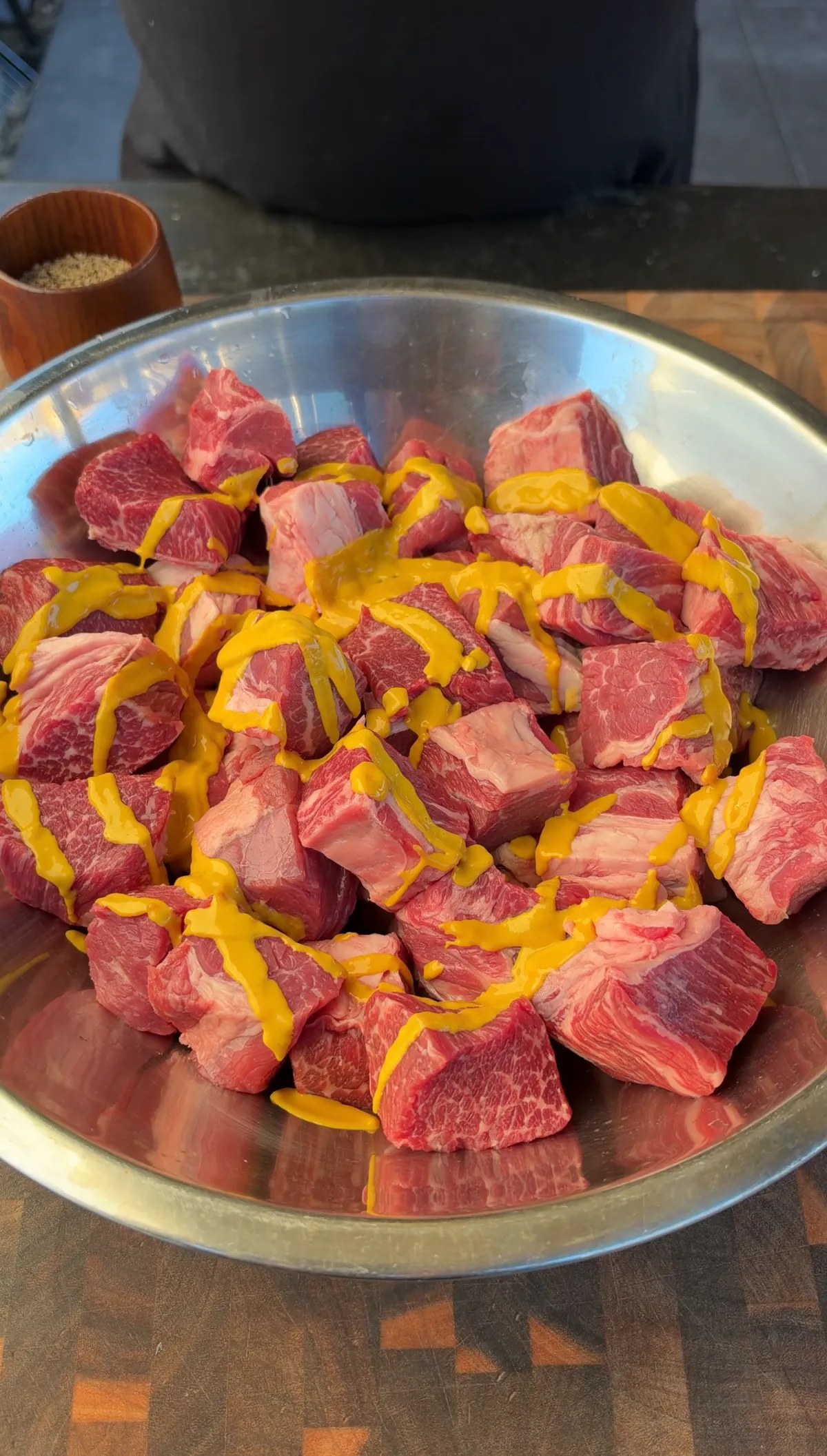 Raw chuck roast cubes in a steel bowl drizzled with yellow mustard binder, ready to season and smoke