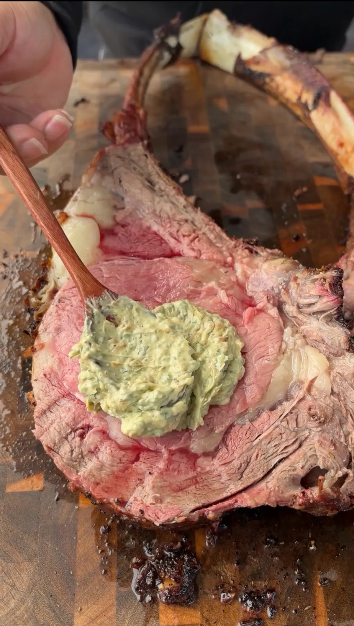 Roasted garlic and onion compound butter dolloped onto the cut surface of a tomahawk prime rib resting on a cutting board