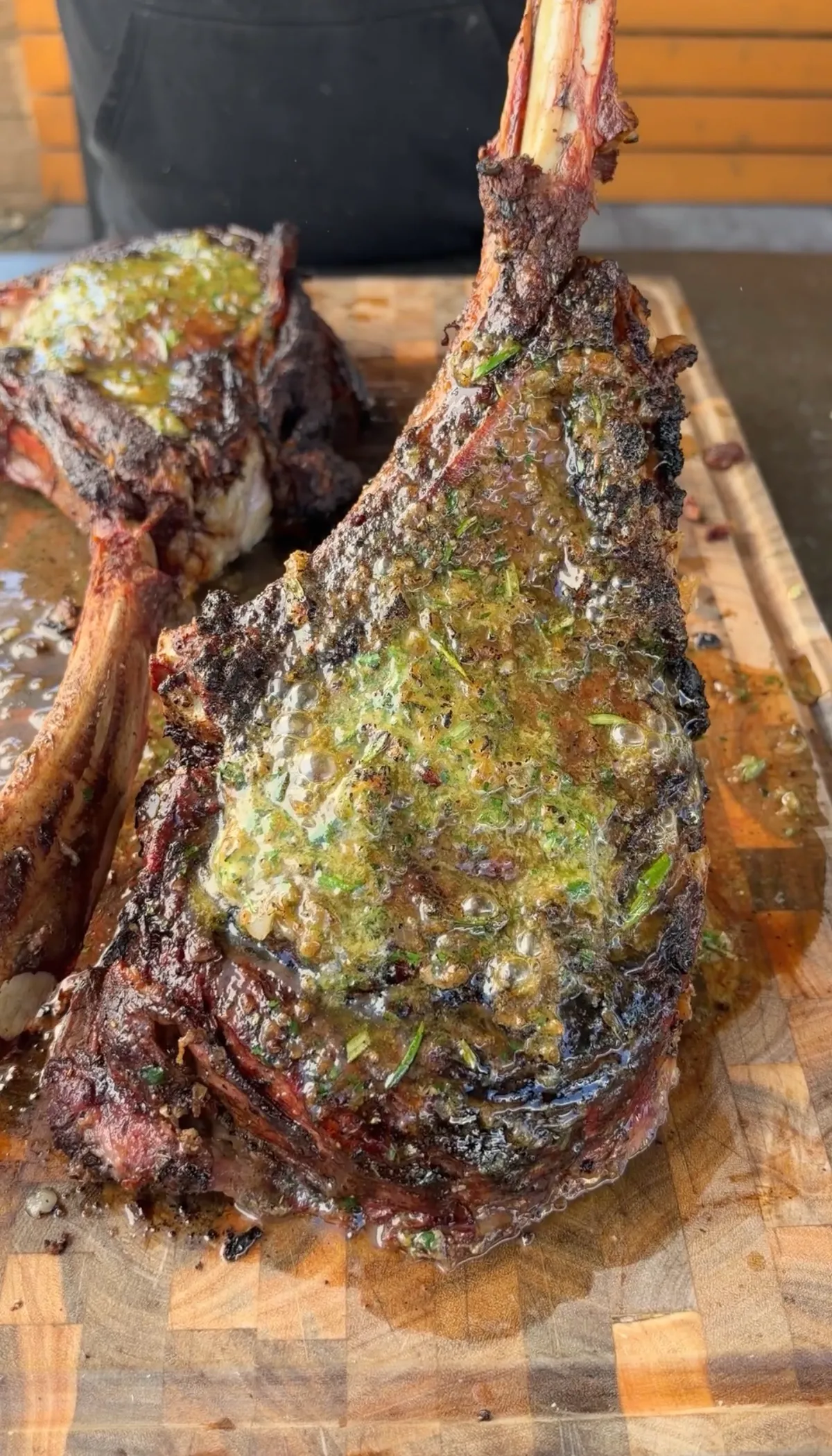 Tomahawk prime rib resting on a cutting board, bone up, with roasted garlic and onion compound butter melting over the crust