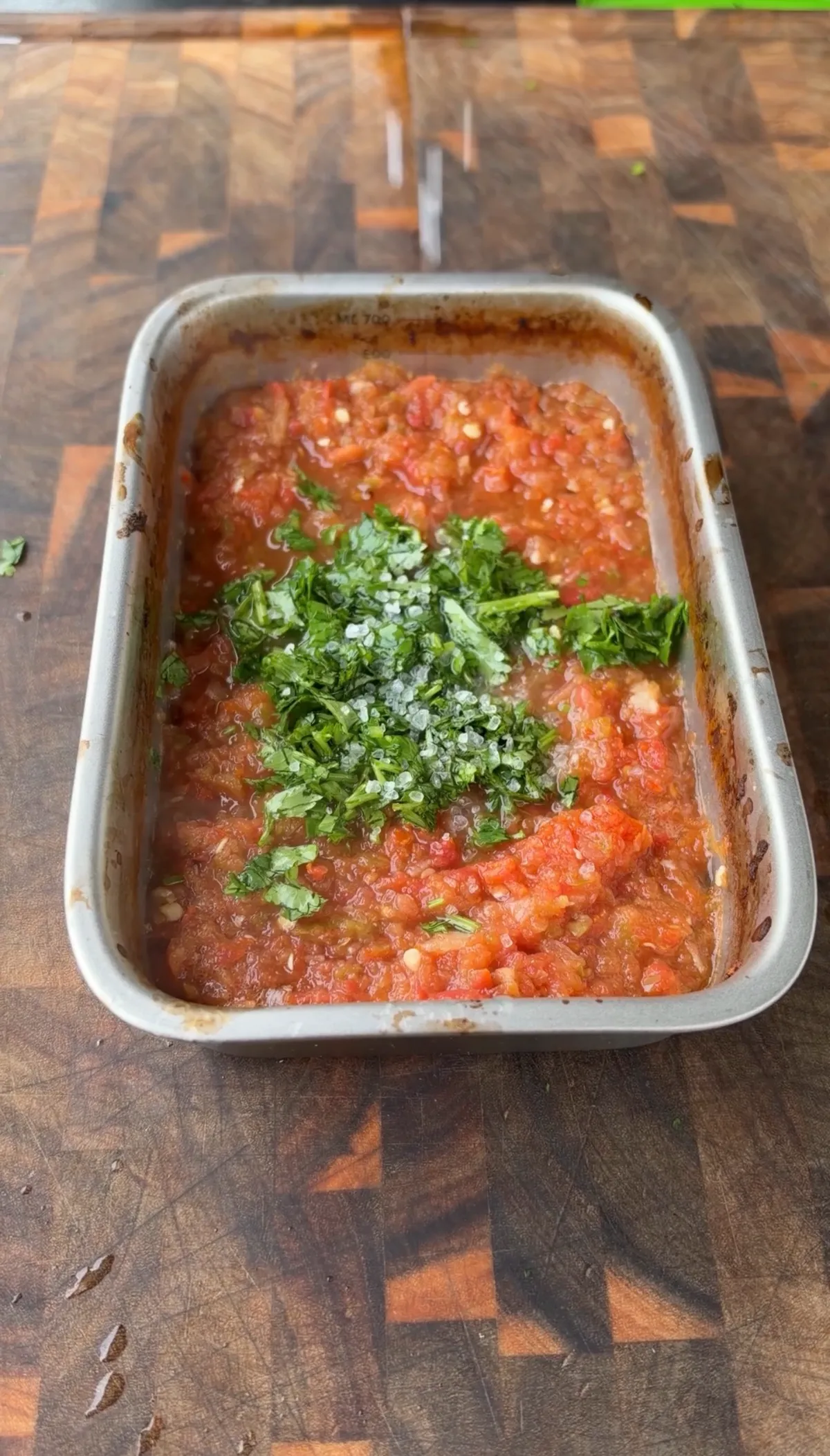 Homemade salsa reduced in a roasting pan topped with fresh chopped cilantro and coarse salt on a wooden cutting board