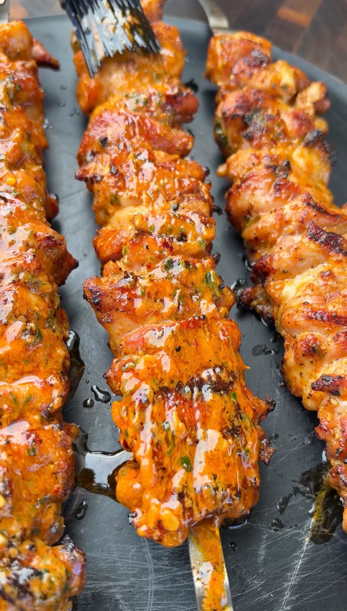 Juicy grilled chicken thigh skewers being basted with garlicky cowboy butter on a dark grill pan