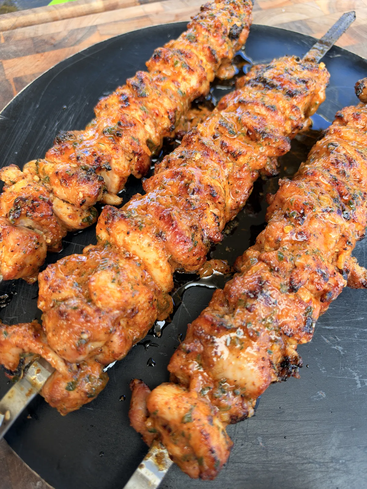Juicy grilled chicken thigh skewers coated in cowboy butter on a black serving tray, charred and glistening