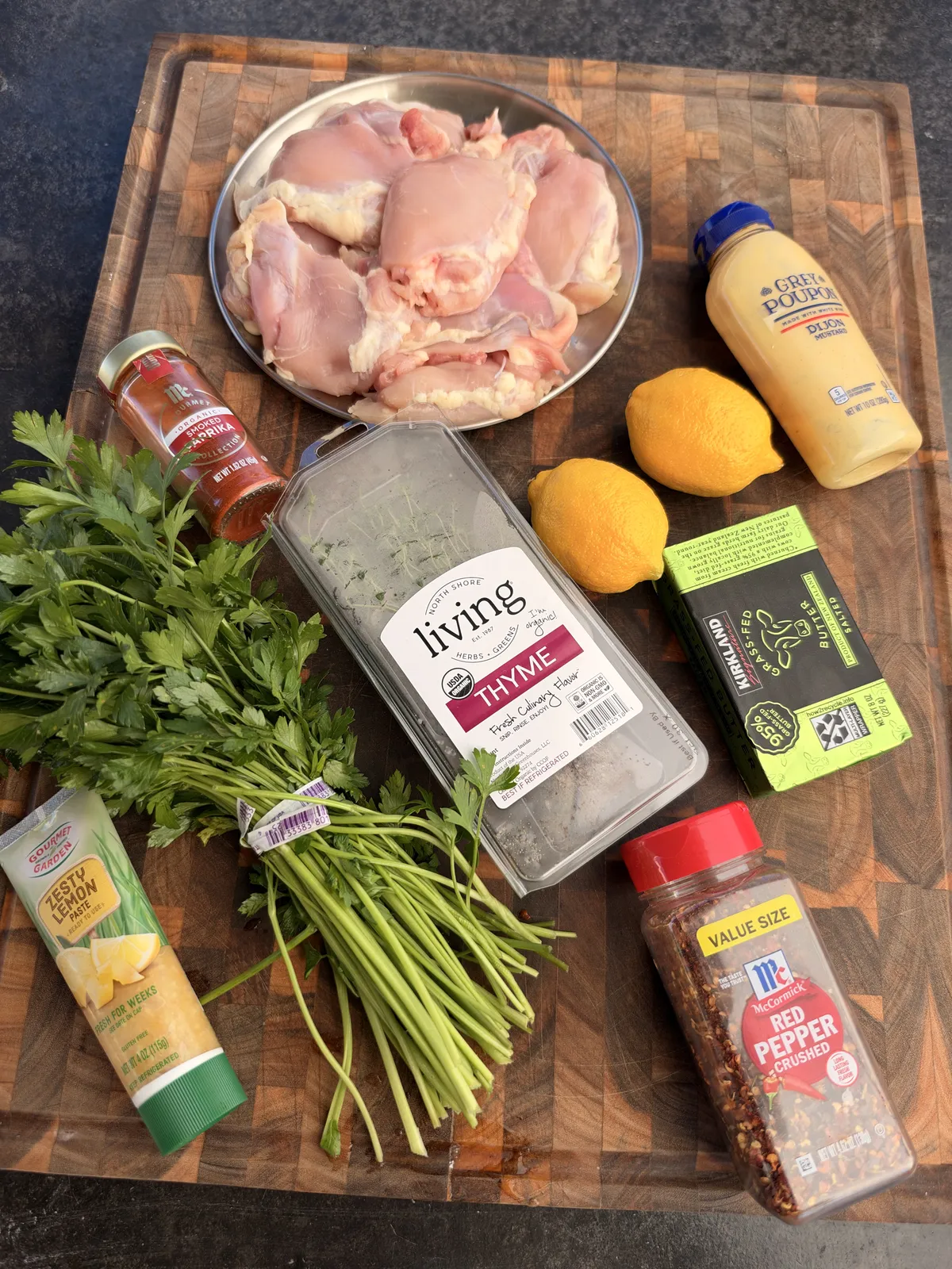 Flat lay of cowboy butter chicken skewer ingredients: raw chicken thighs, butter, Dijon mustard, lemons, thyme, parsley, paprika, and red pepper flakes