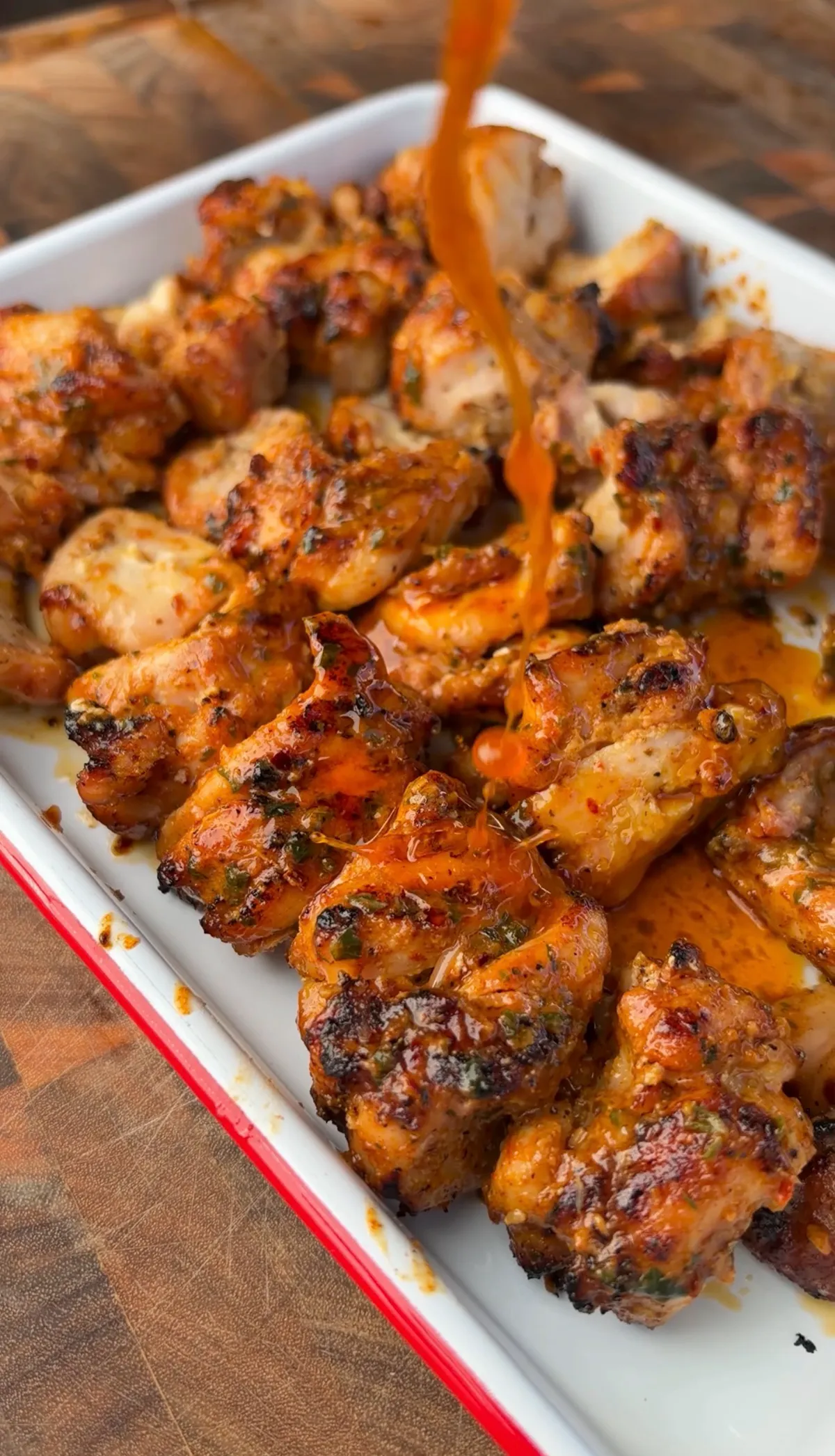 Cowboy butter sauce being poured over grilled chicken thigh skewers on a white serving platter