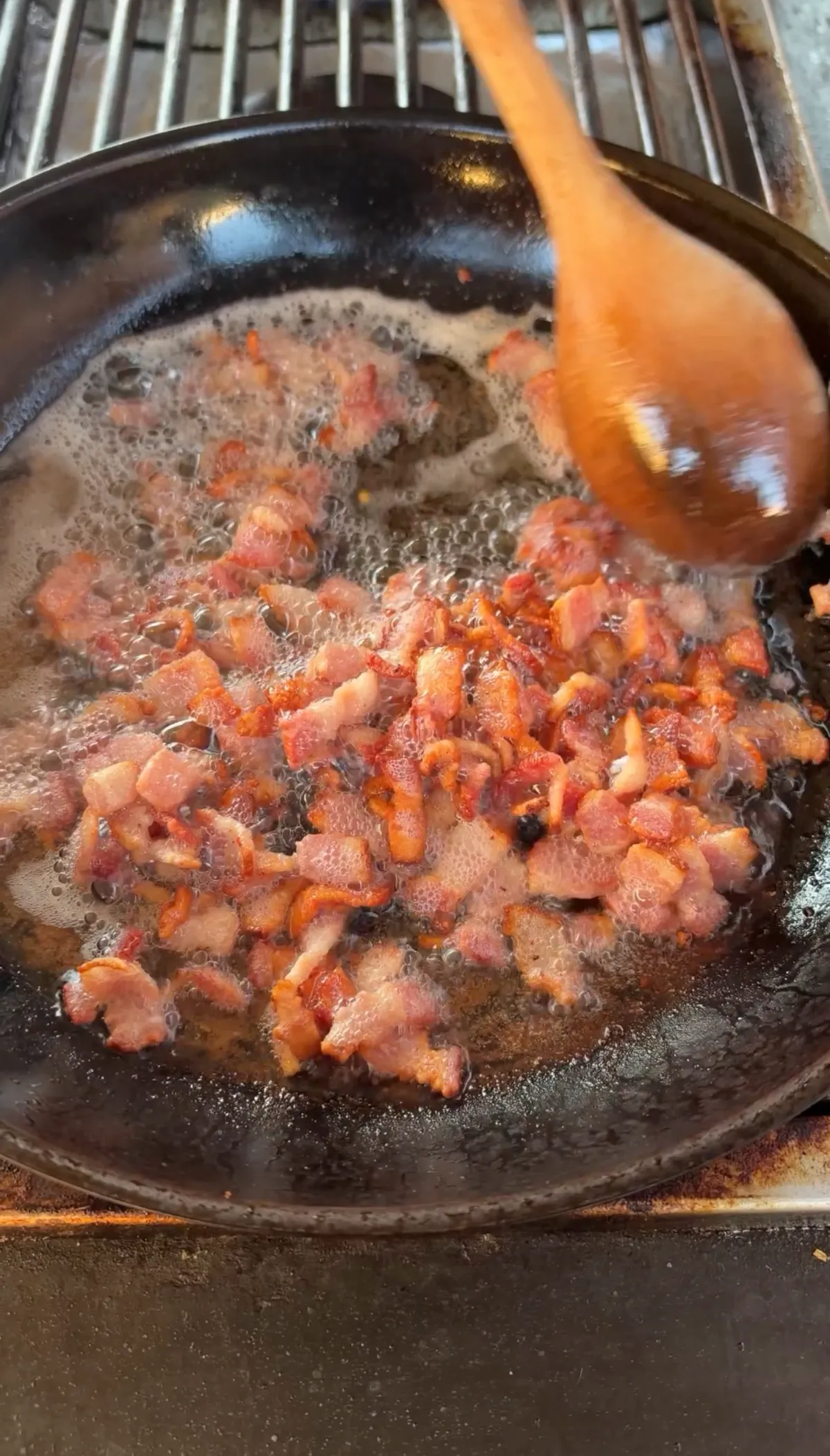Diced bacon cut into ¼-inch pieces frying in a cast iron skillet, stirred with a wooden spoon