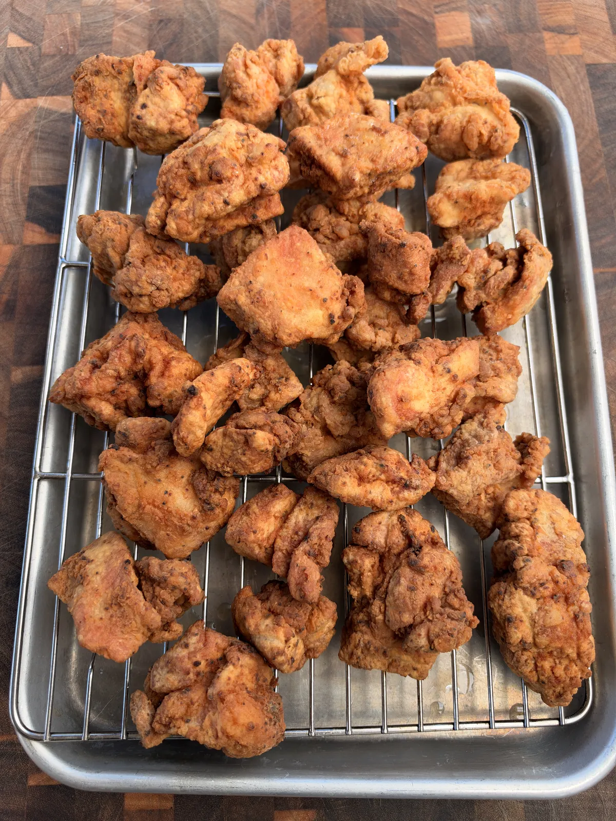 Golden-brown crispy fried chicken thigh nuggets resting on a wire rack over a sheet pan after frying