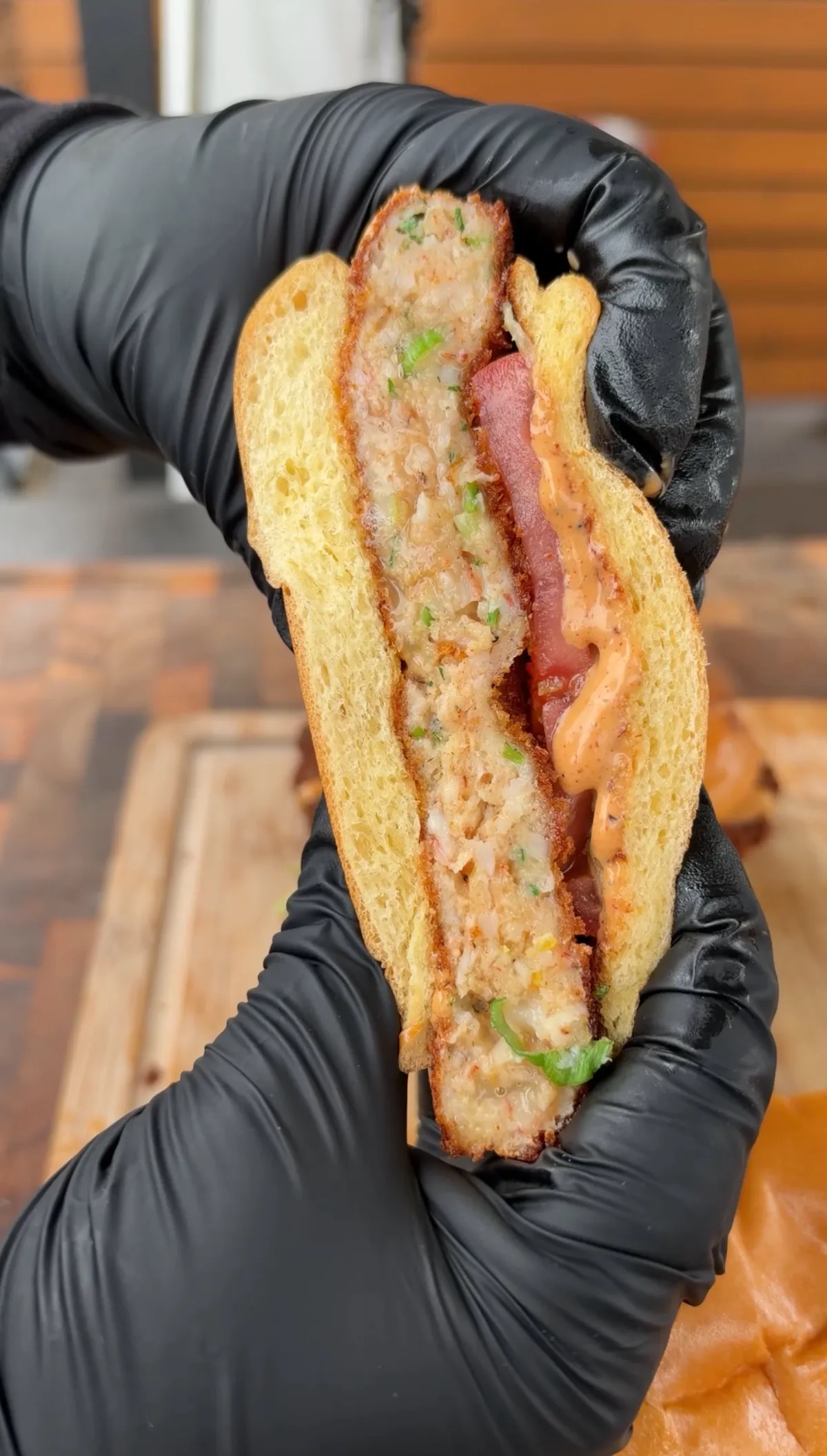 Cross-section of a crispy fried shrimp burger on toasted brioche bun with chipotle mayo, sliced tomato, and lettuce