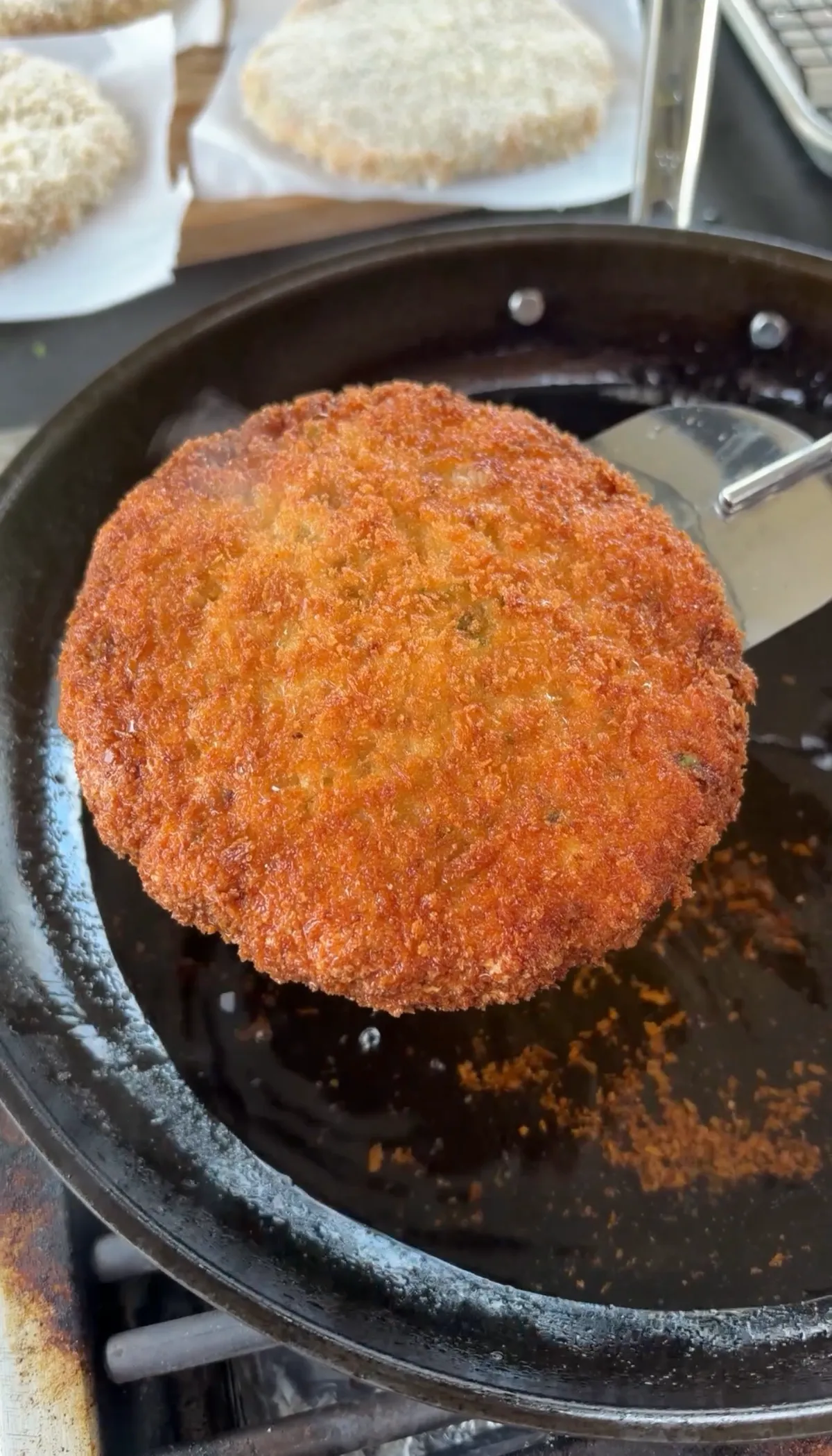 Golden crispy panko-breaded shrimp burger patty being lifted from frying pan with spatula at 350°F