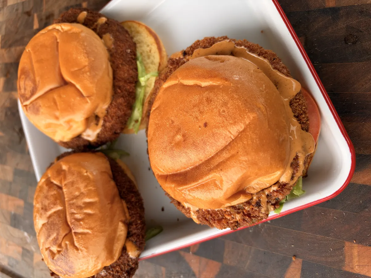 Three crispy fried shrimp burgers on toasted brioche buns with chipotle mayo and lettuce on a white tray