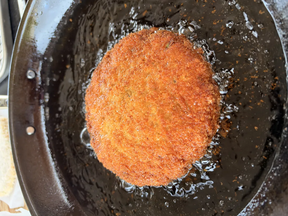 Breaded shrimp burger patty frying in hot neutral oil at 350°F in a shallow pan, golden brown panko crust