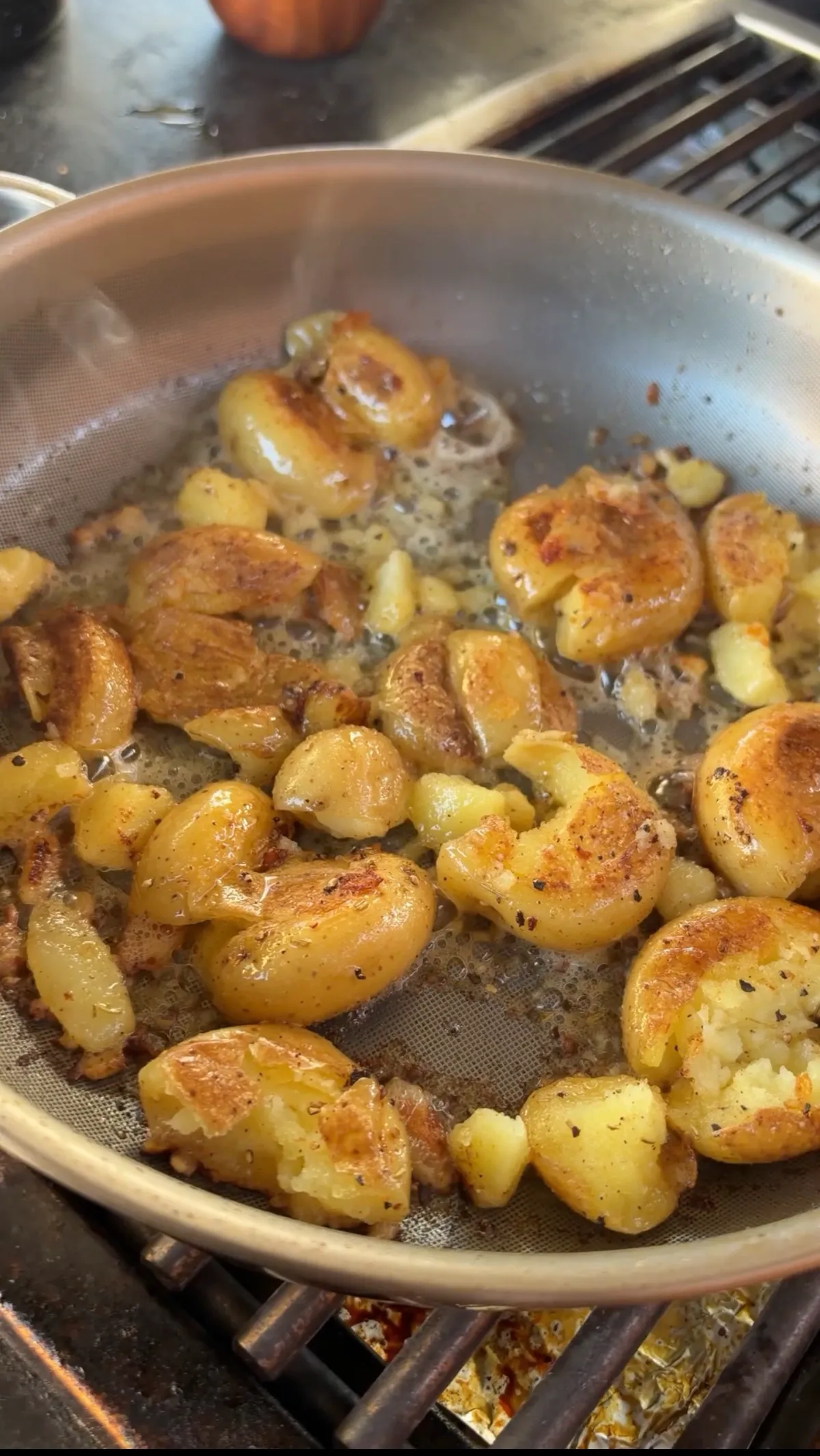 Golden smashed potatoes searing in bubbling butter in a stainless pan, crispy and caramelized on the outside