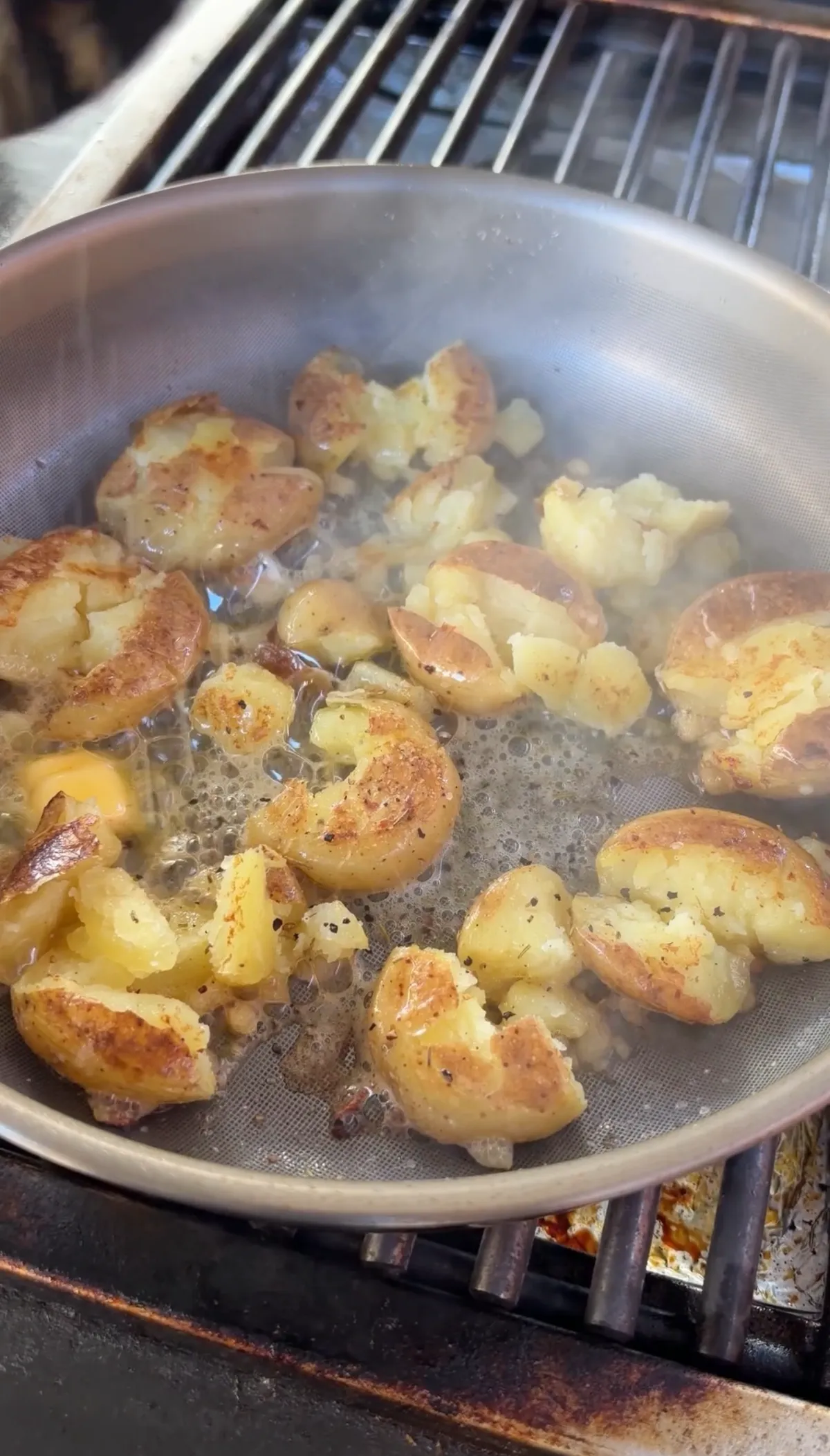 Golden crispy smashed potatoes searing in butter in a stainless pan on a grill grate
