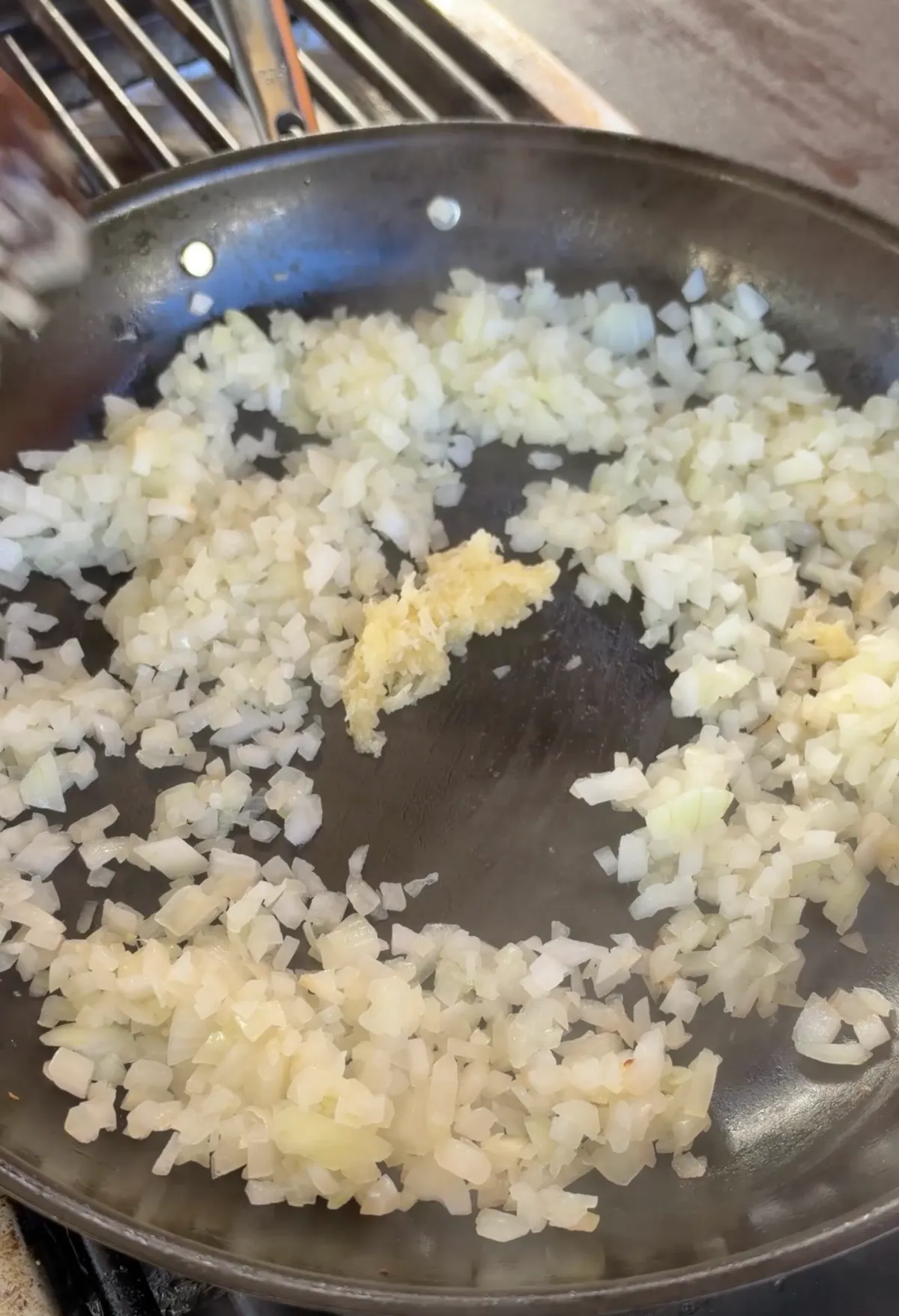 Diced onions sweating in a skillet with minced garlic added to the center, cooking down for smash burrito filling