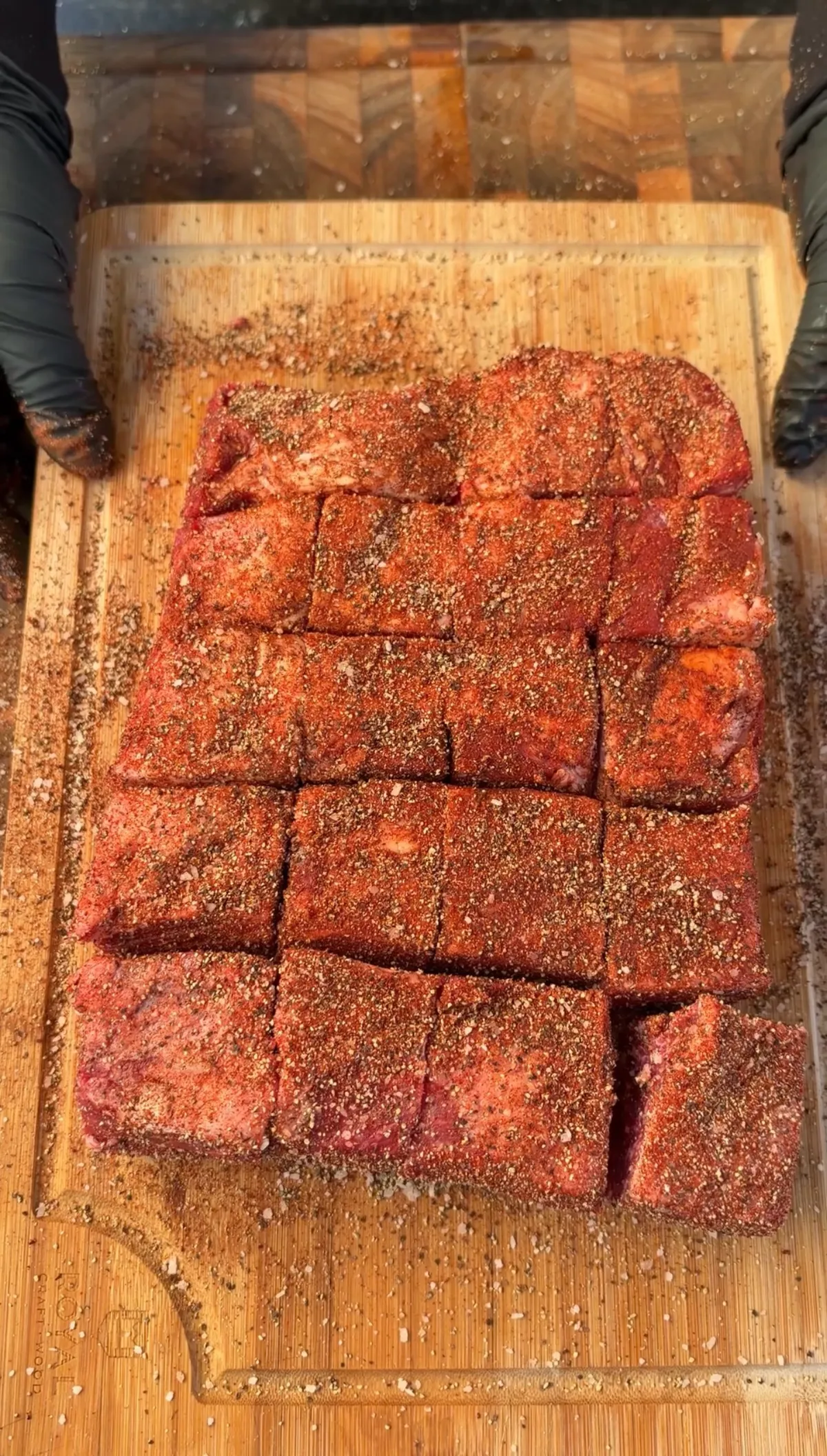 Grid of raw beef short rib cubes heavily coated in red dry rub seasoning on a wooden cutting board