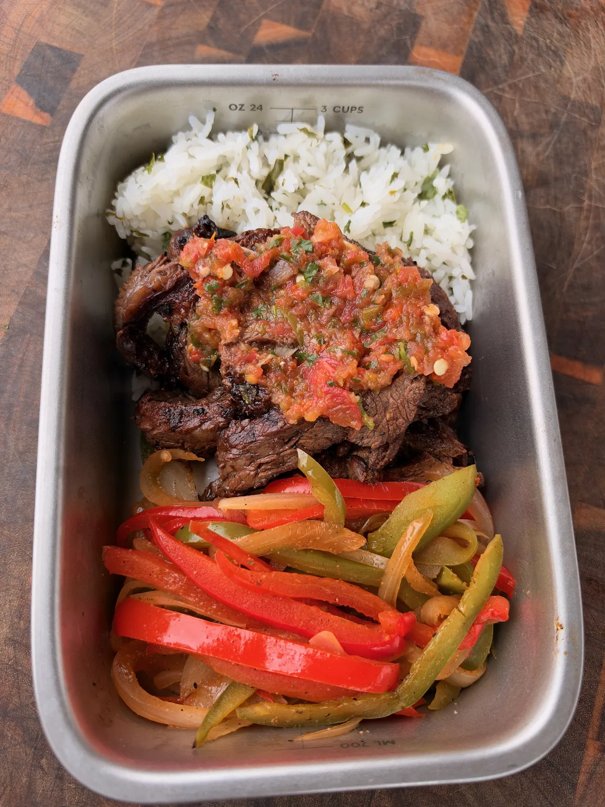 Meal prep container with grilled skirt steak topped with homemade salsa, cilantro lime rice, and charred bell peppers and onions