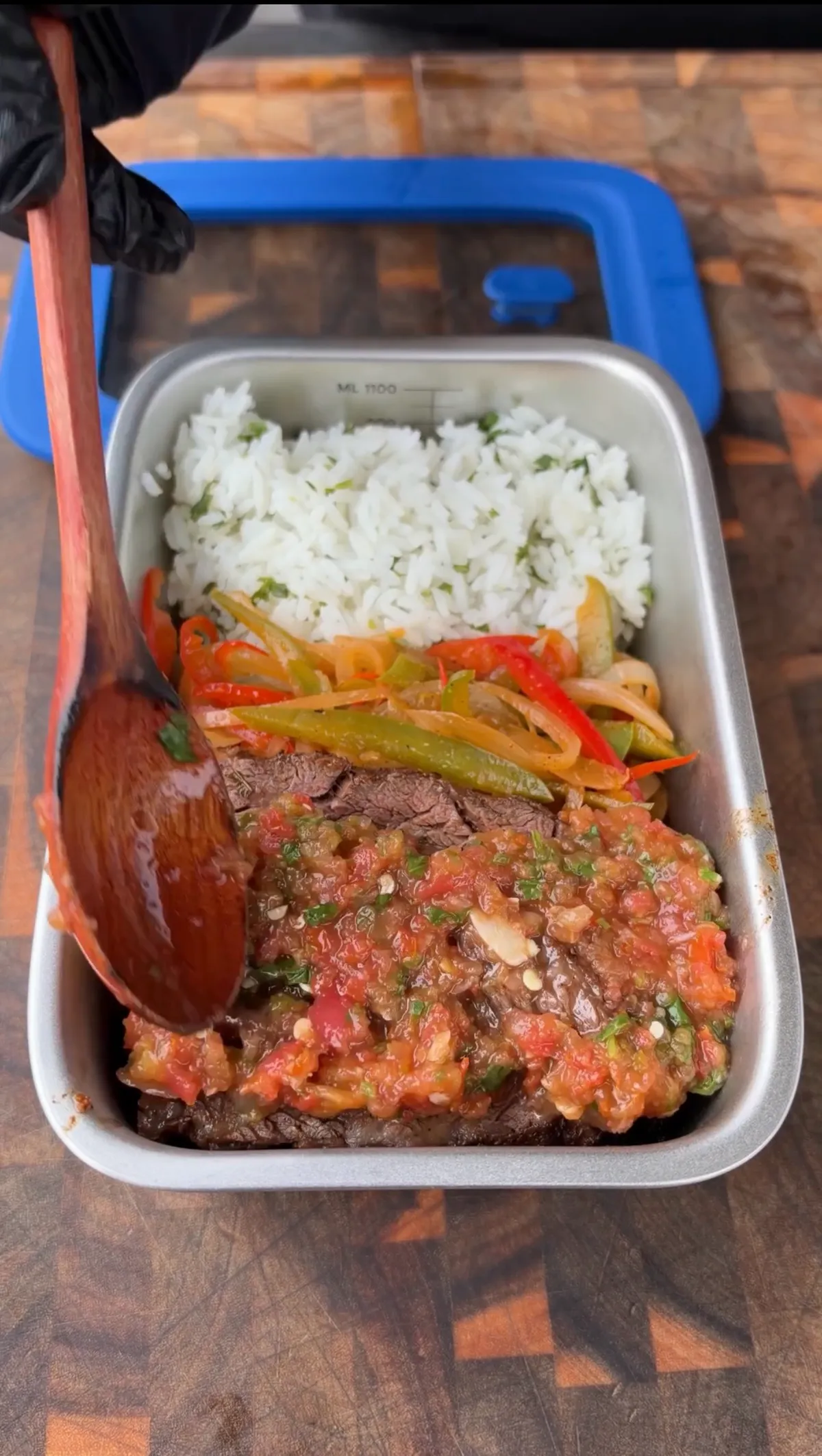 Skirt steak fajita meal prep container with homemade salsa being spooned over meat, charred peppers, onions, and cilantro lime rice
