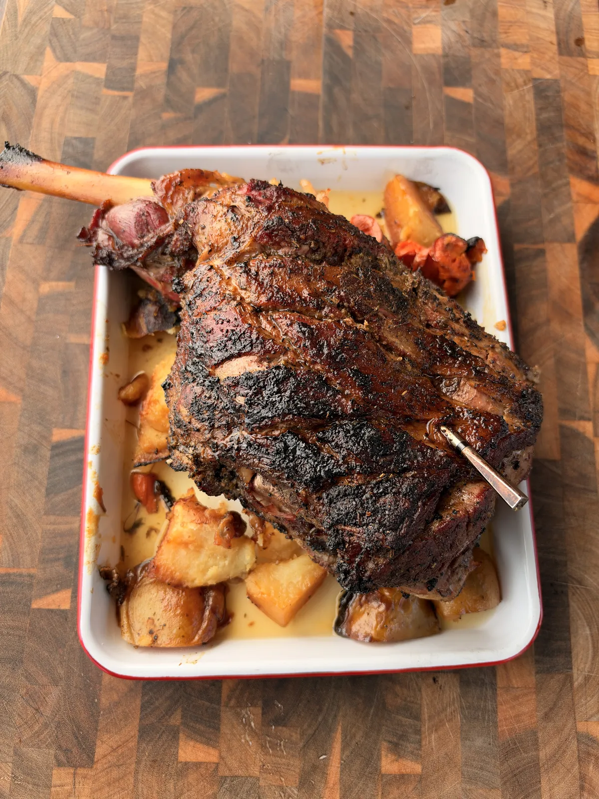 Greek style braised leg of lamb fall-apart tender in white enamel roasting tray with Yukon Gold potatoes and carrots