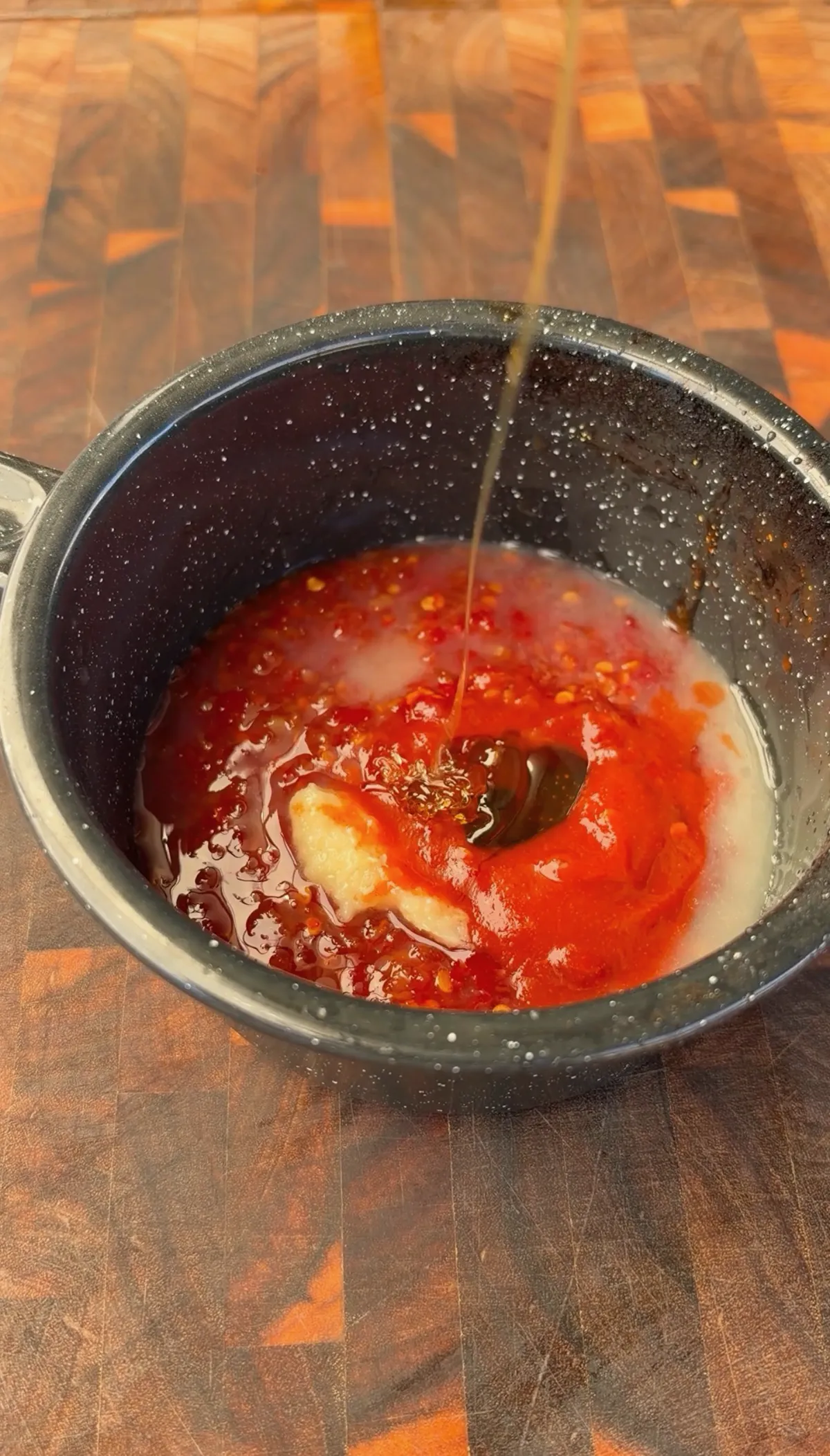 Sweet chili sauce, sriracha, and honey being poured into a small saucepan to make firecracker glaze