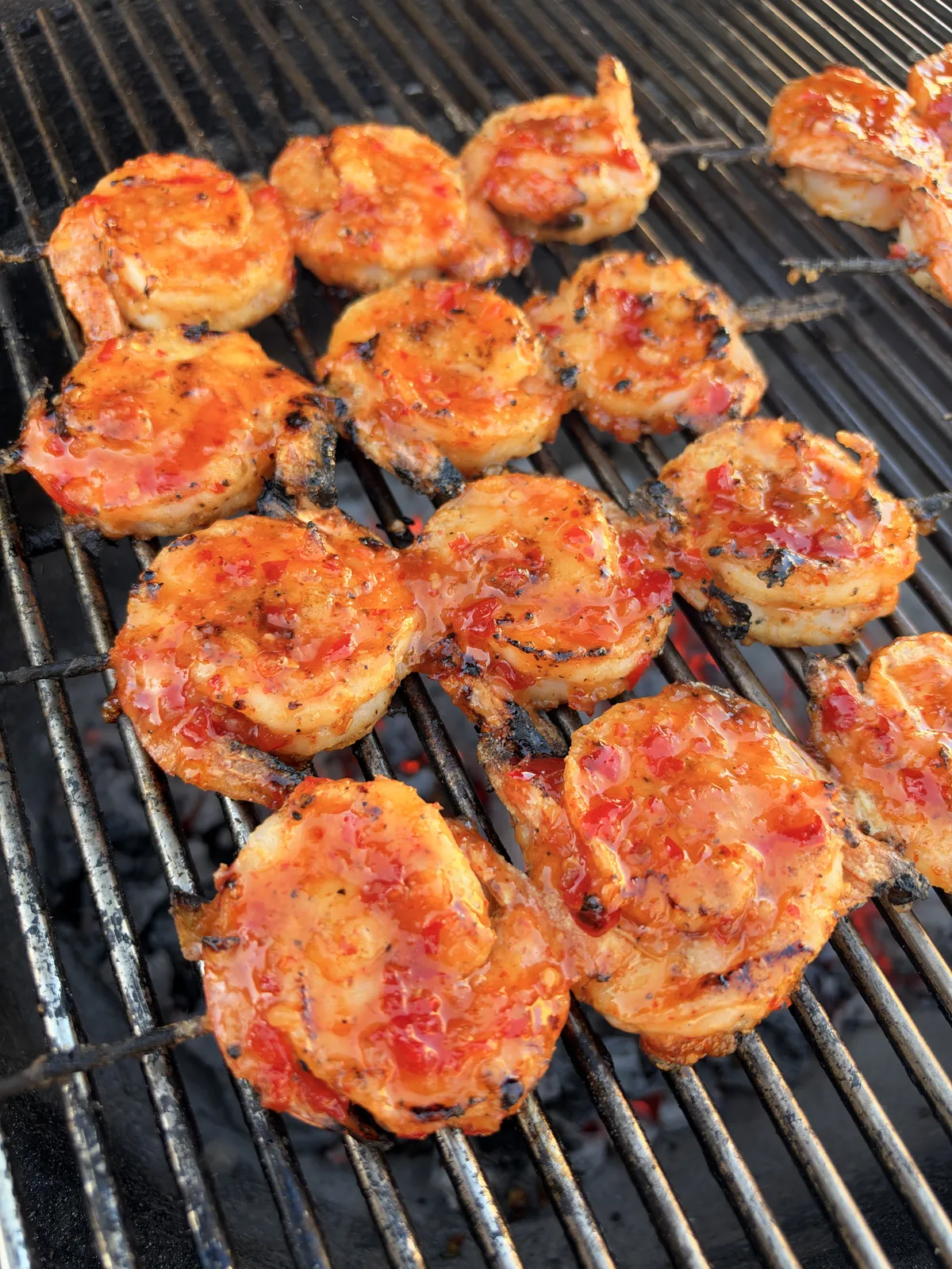 Firecracker grilled shrimp skewers coated in sticky sweet chili sriracha glaze caramelizing over hot grill grates