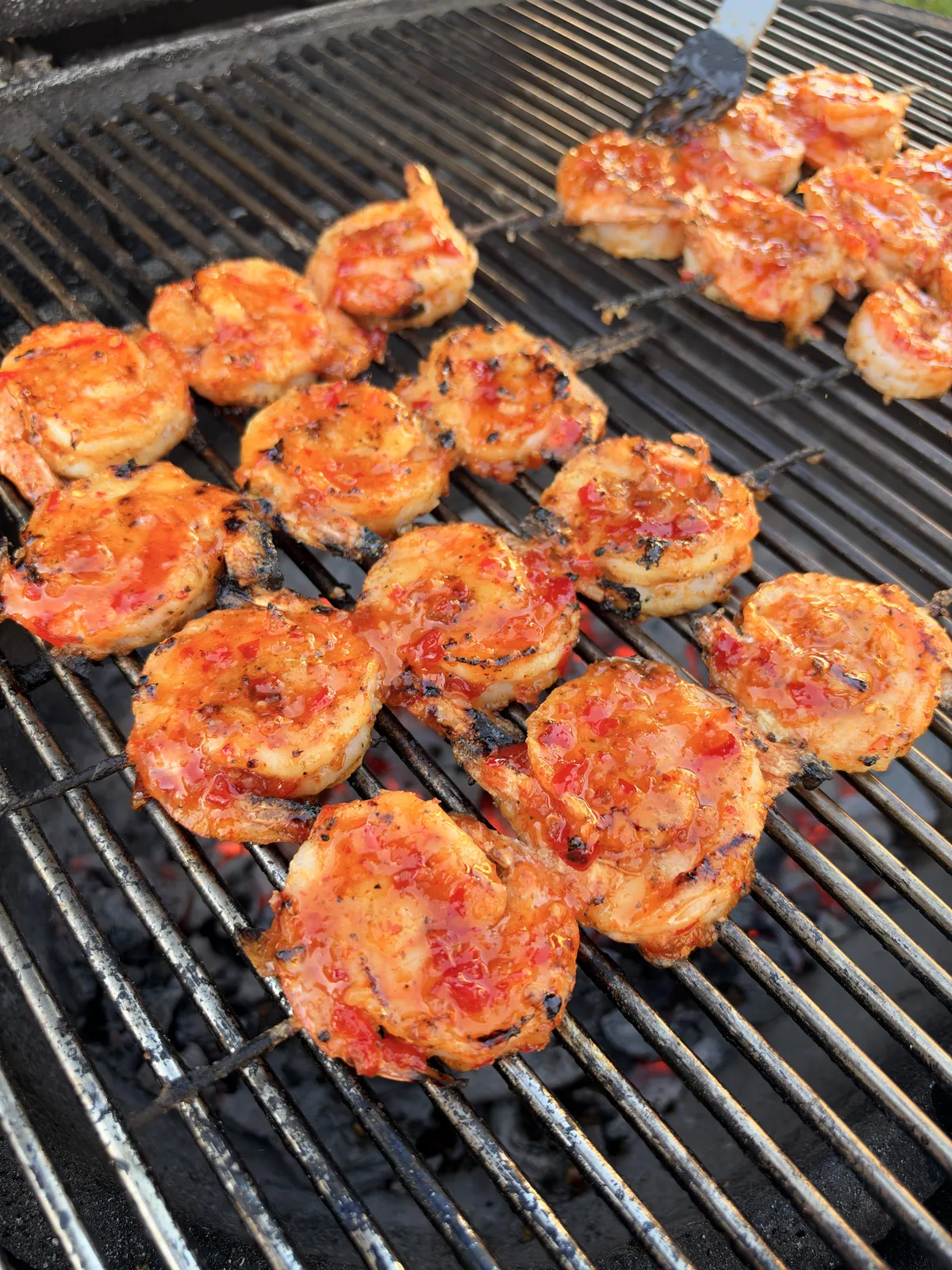 Firecracker shrimp skewers coated in sticky sweet chili sriracha glaze grilling over high heat on charcoal grill grates