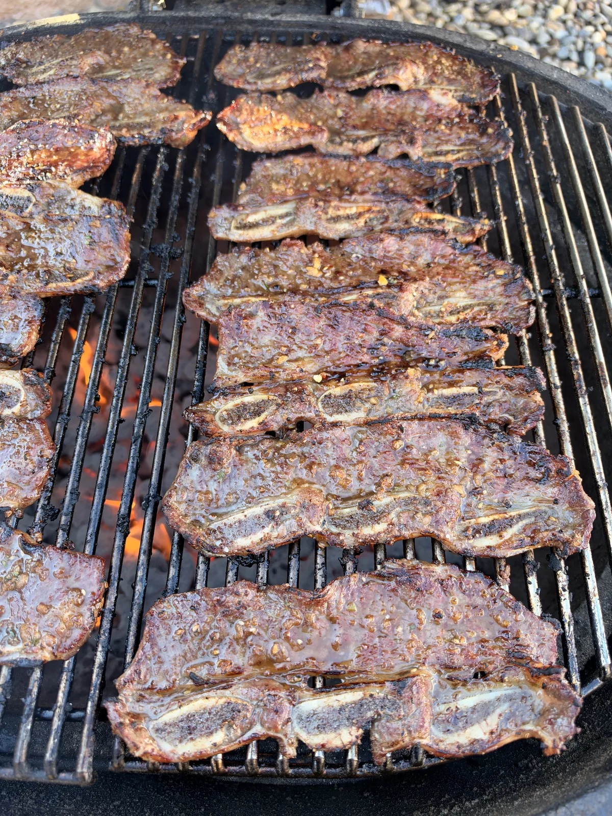 Flanken-cut beef short ribs grilling over direct high heat on a charcoal grill, caramelizing in kalbi marinade