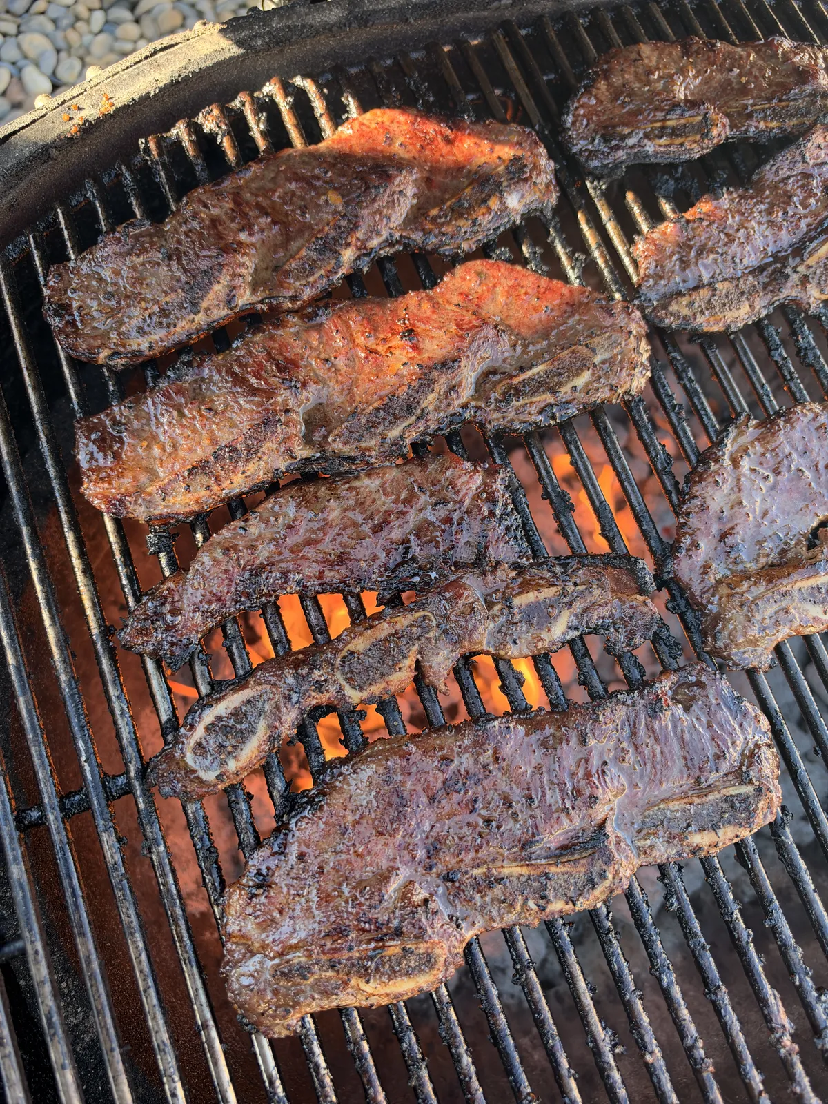 Korean kalbi beef short ribs grilling over direct high heat with visible flames and caramelized char on cast iron grates