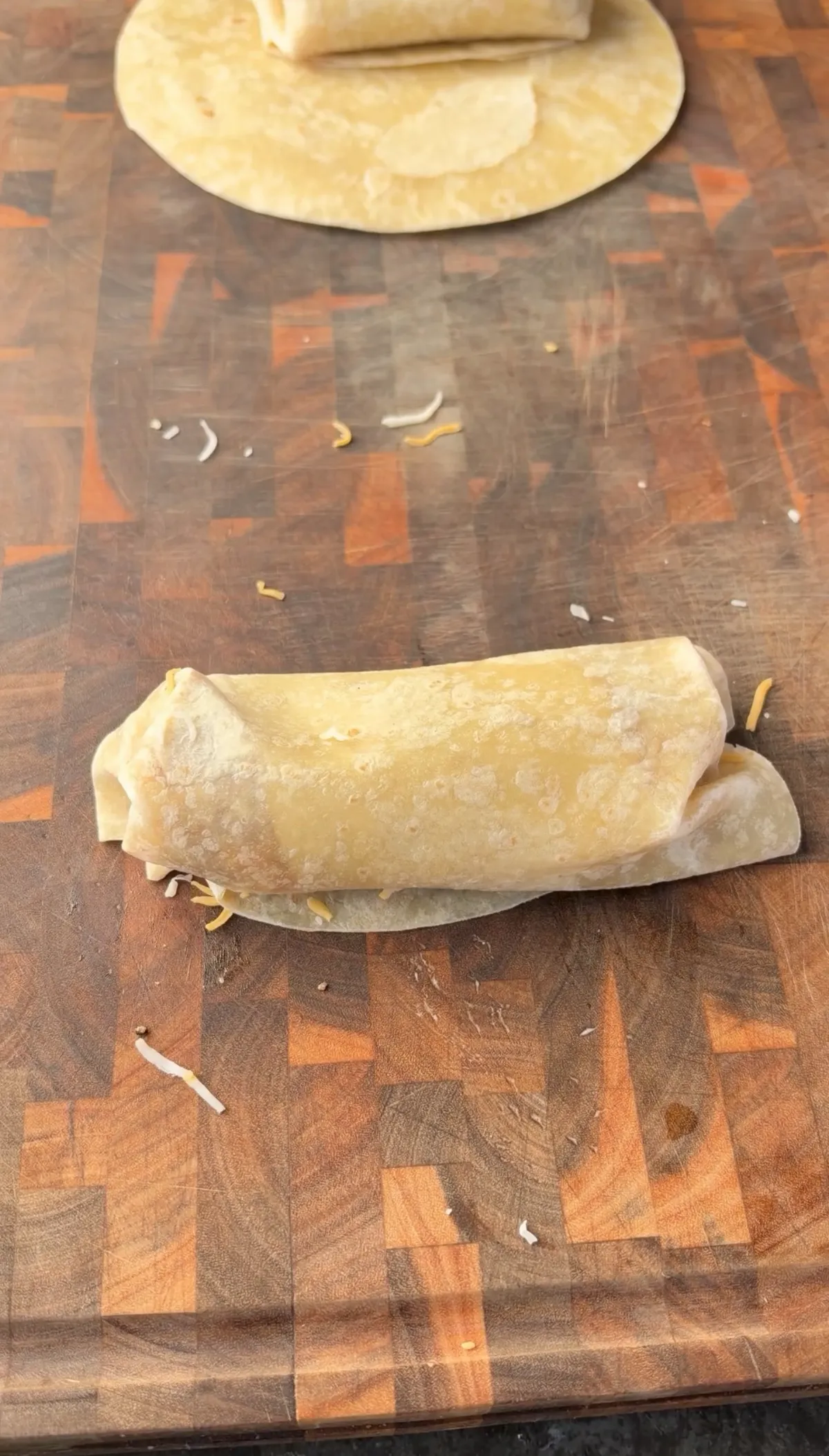 Flour tortilla burrito stuffed with ground beef, pepper jack, and Colby jack cheese folded tight on a wooden cutting board