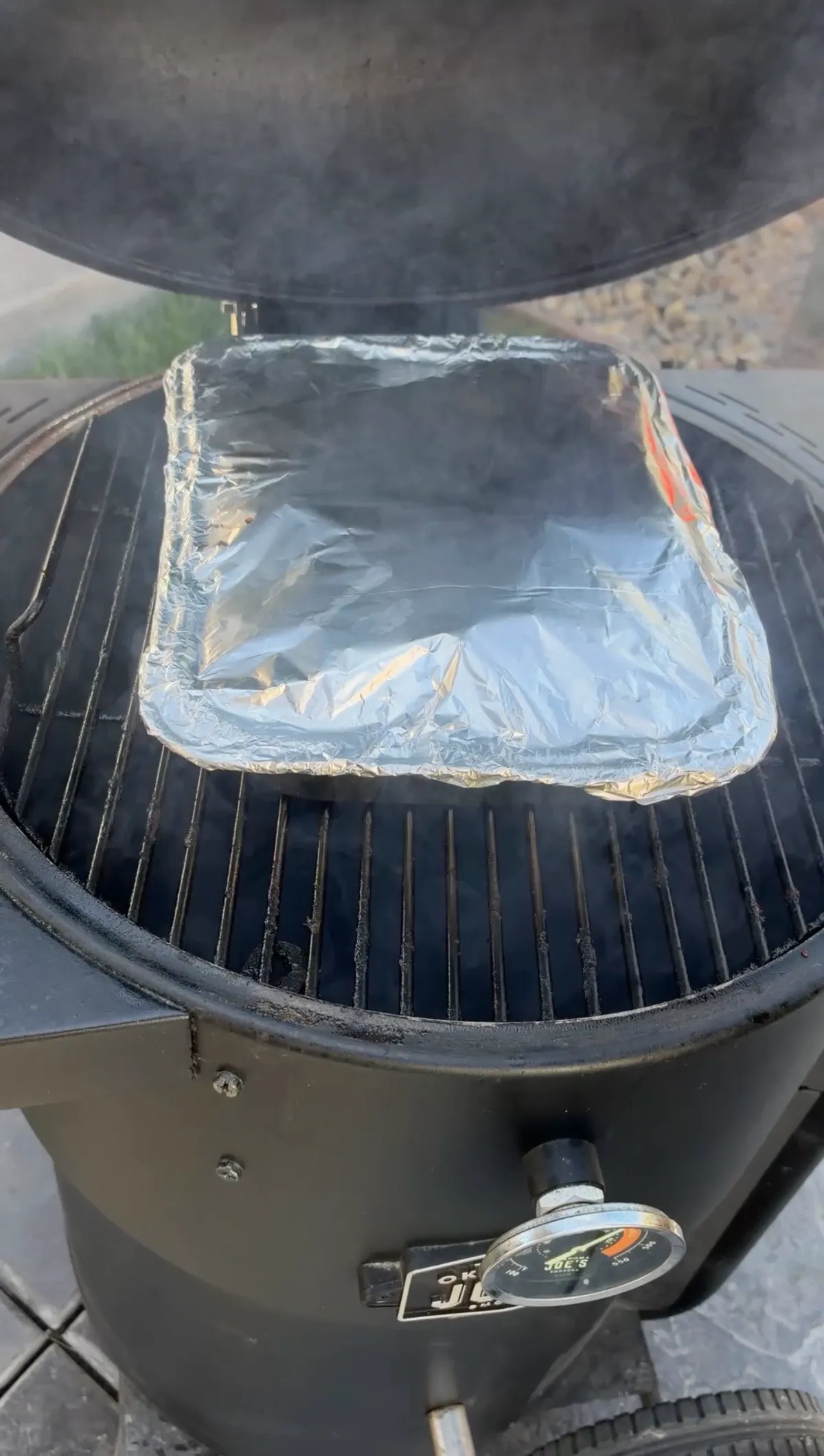Foil-covered tray of St. Louis-style party ribs braising in sticky barbecue sauce on an Oklahoma Joe's smoker