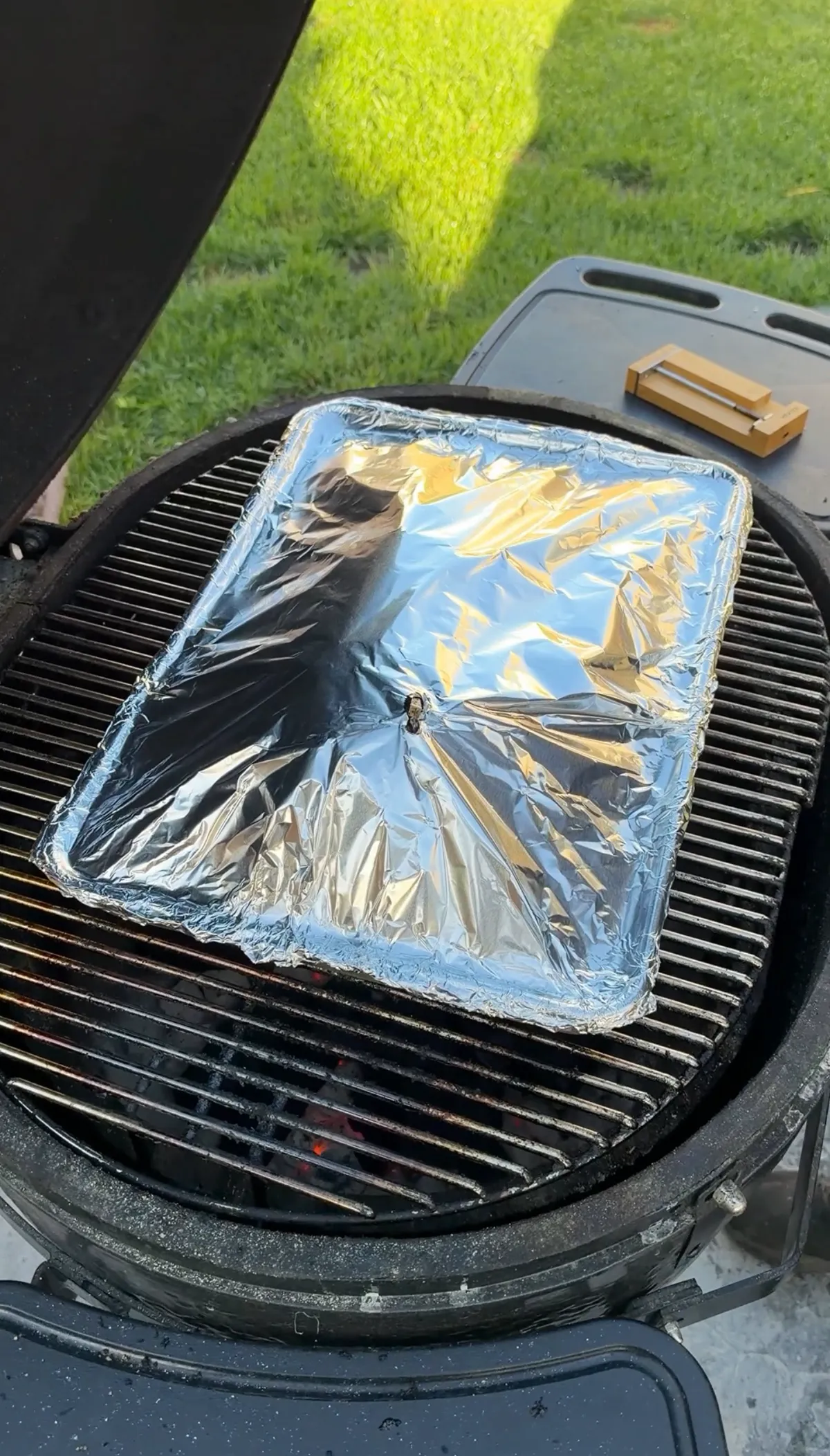 Heavy-duty aluminum foil tightly sealed over roasting tray braising Greek leg of lamb on a charcoal grill