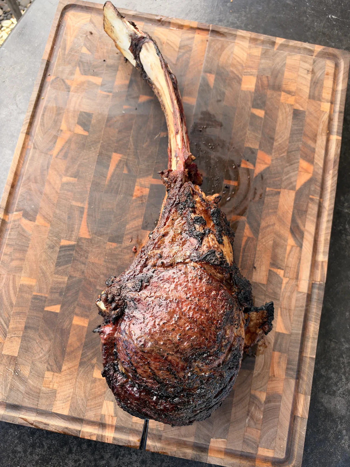 Two-bone prime rib tomahawk with deep seared crust resting on a wood cutting board after grilling