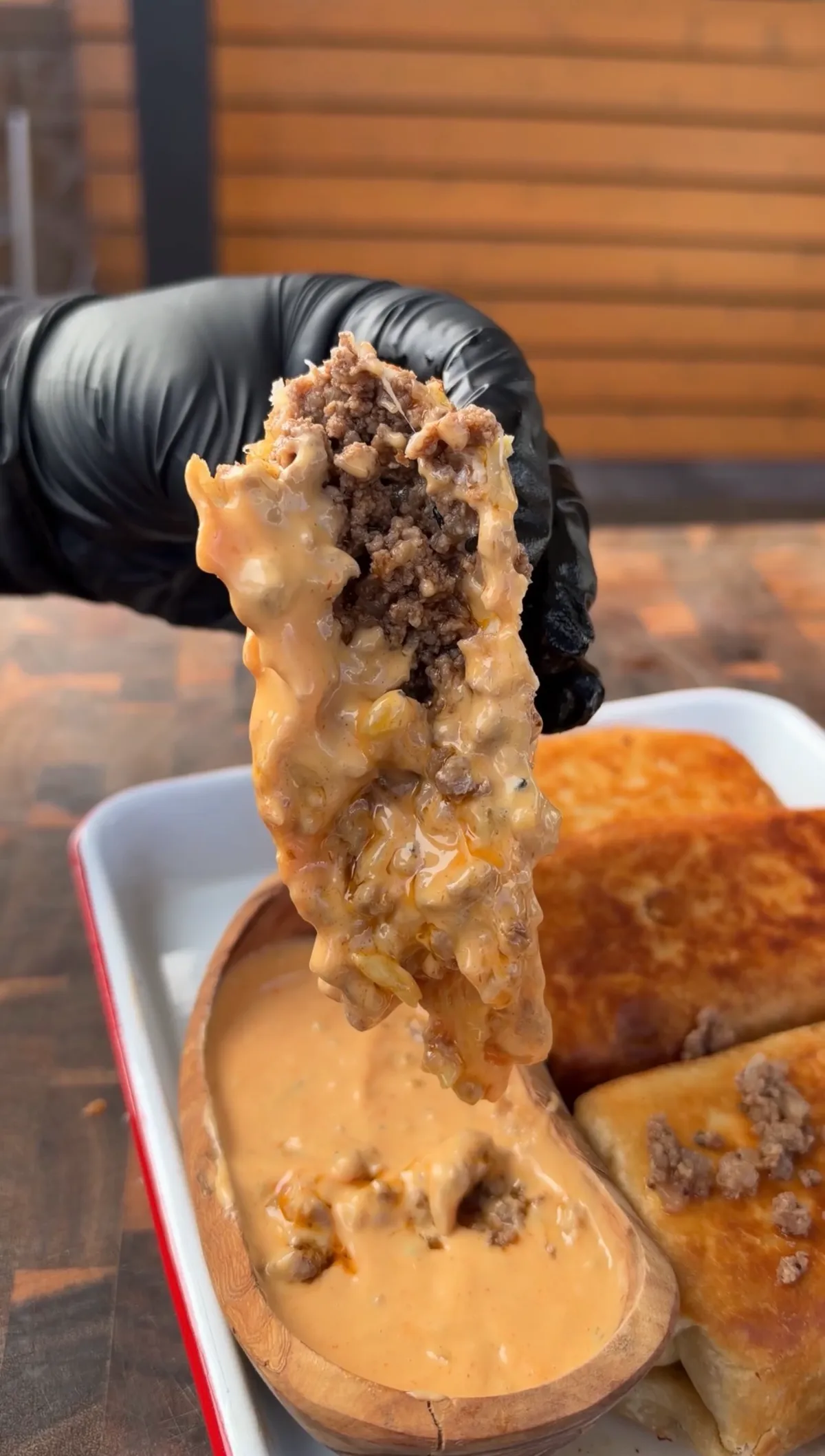 Gloved hand pulling apart a golden fried burrito with ground beef, pepper jack, and Colby jack cheese dripping into burger sauce