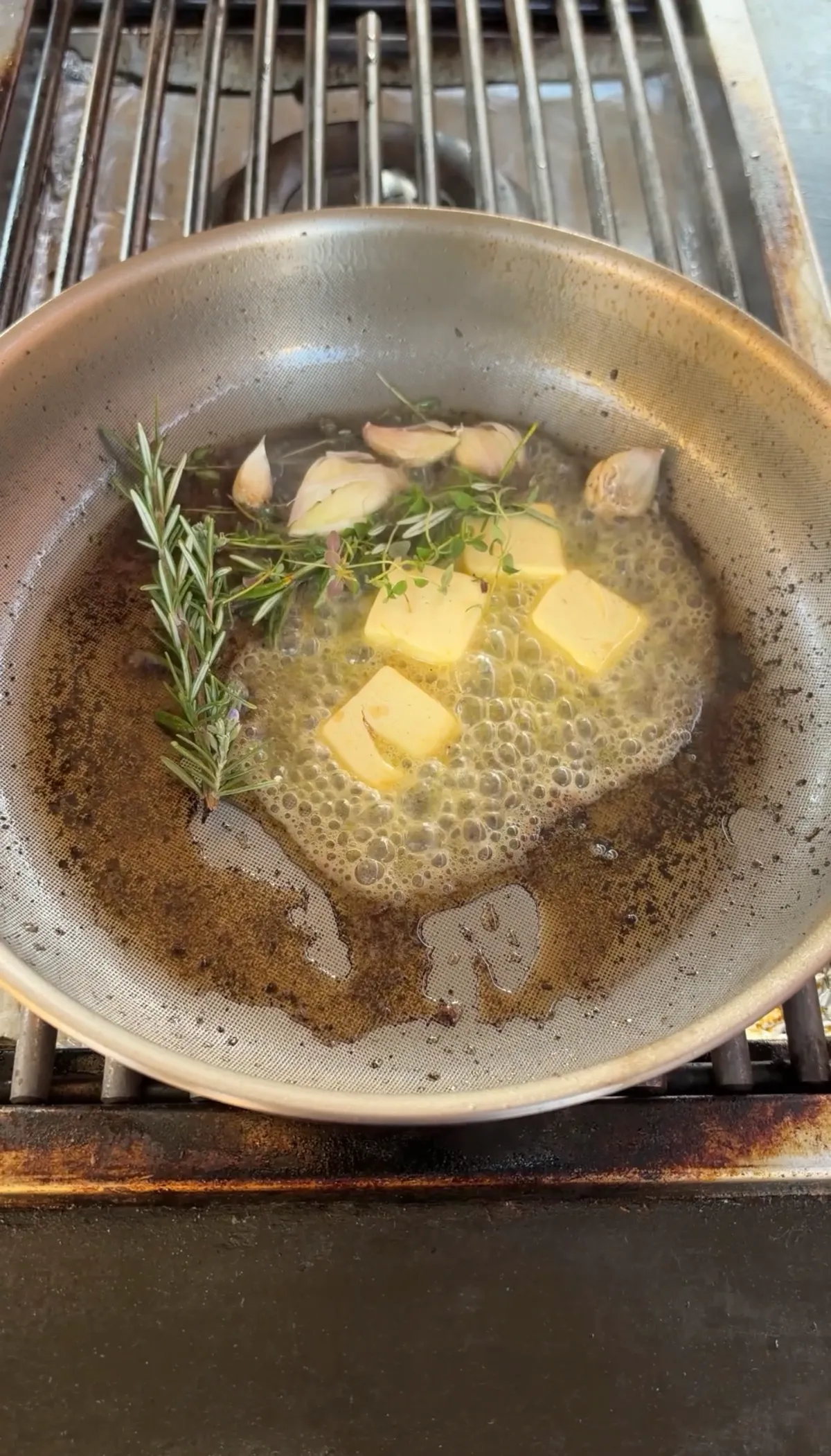 Butter cubes melting in pan with smashed garlic cloves, fresh rosemary, and thyme sprigs for garlic herb butter