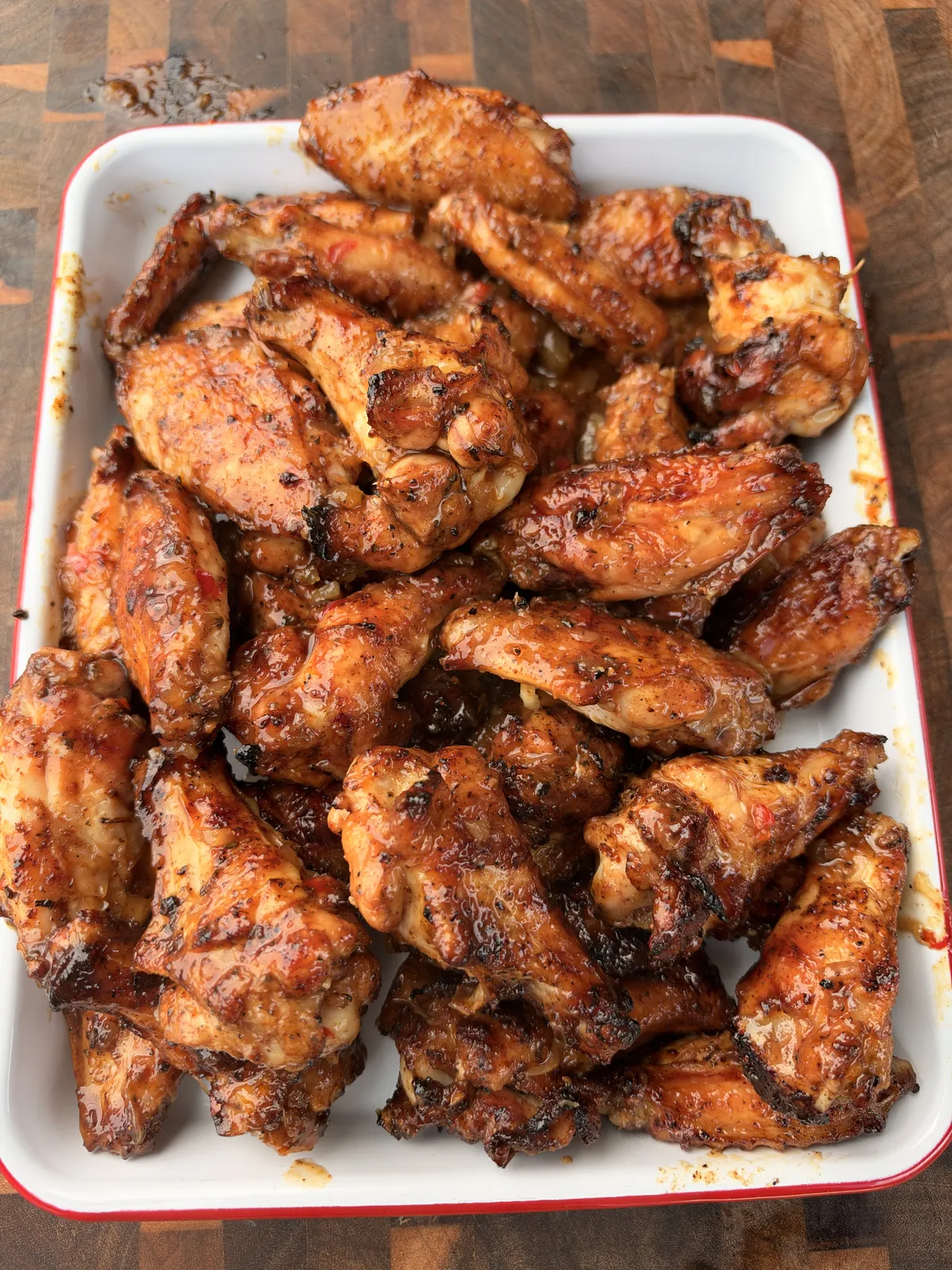 Pineapple habanero grilled chicken wings coated in sticky sweet-and-spicy glaze, piled on a white enamel tray