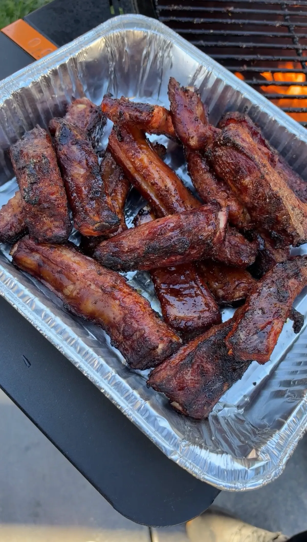 Pile of sticky smoked St. Louis-style barbecue party ribs coated in glossy brown sugar honey BBQ sauce in a foil tray