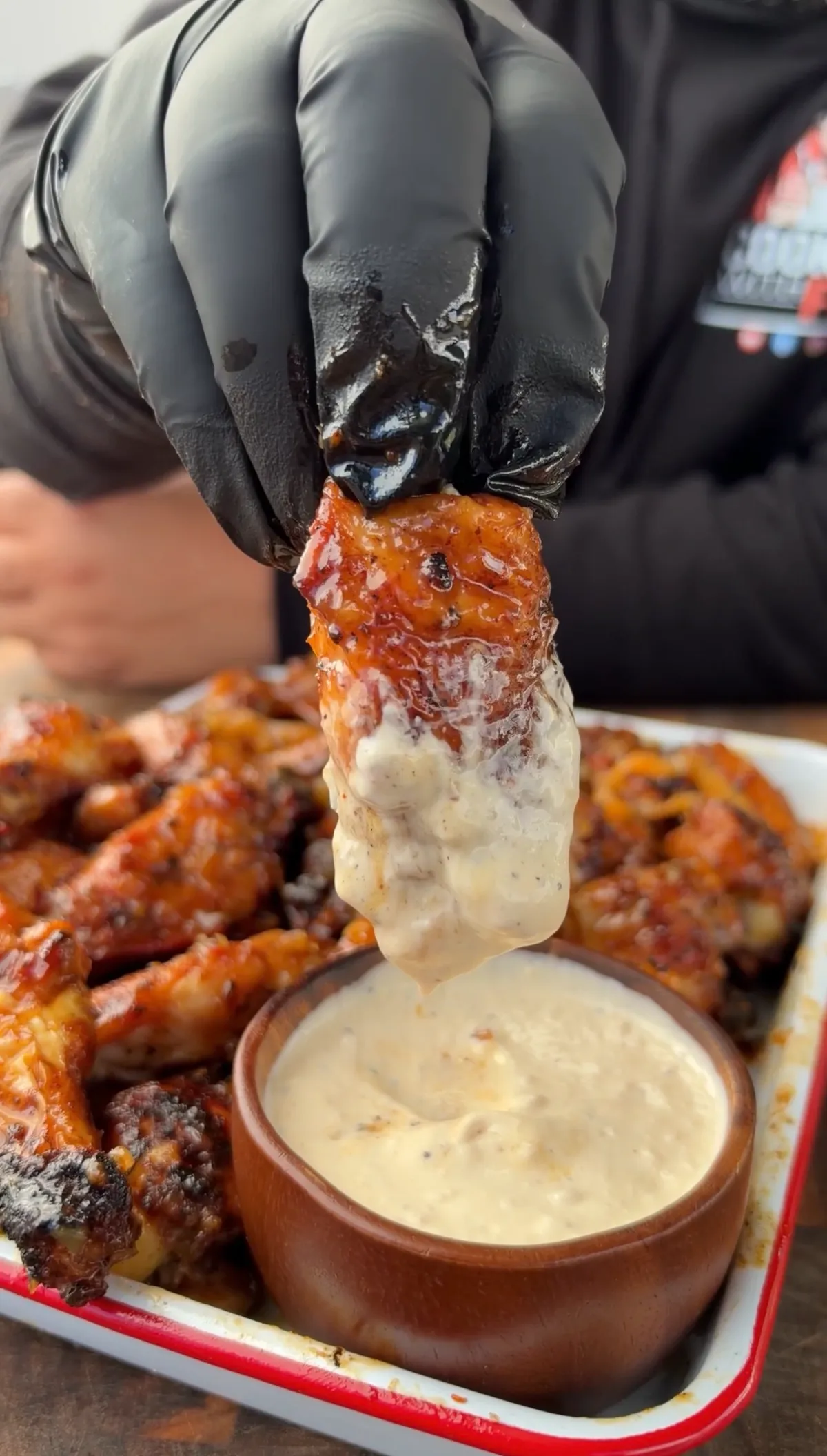 Gloved hand dipping a sticky pineapple habanero glazed chicken wing into a small cup of ranch dressing