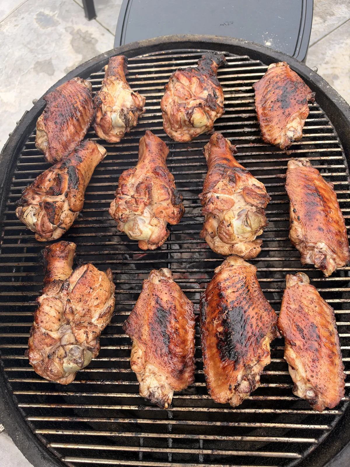 12 grilled BBQ turkey wing pieces with caramelized sauce on a round charcoal grill grate