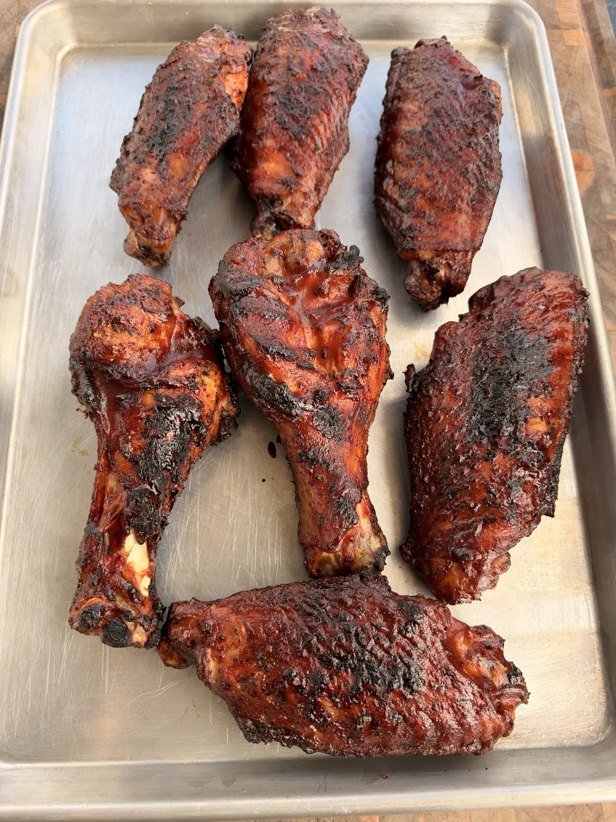 Seven grilled BBQ turkey wings with caramelized tacky glaze arranged on a stainless steel sheet pan