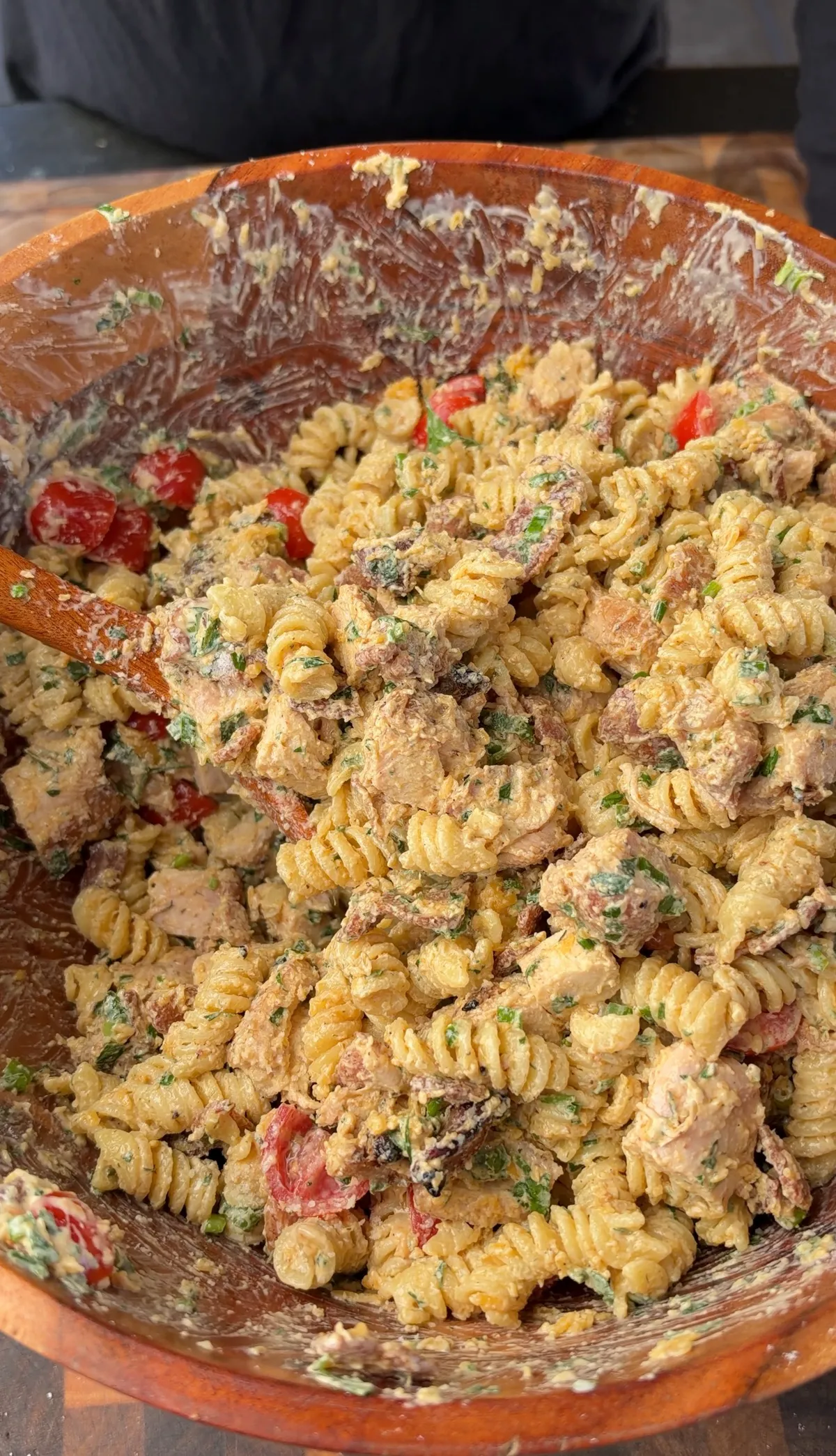 Rotini pasta salad with grilled chicken thighs, crispy bacon, cherry tomatoes, cheddar, and chipotle ranch in a wooden bowl