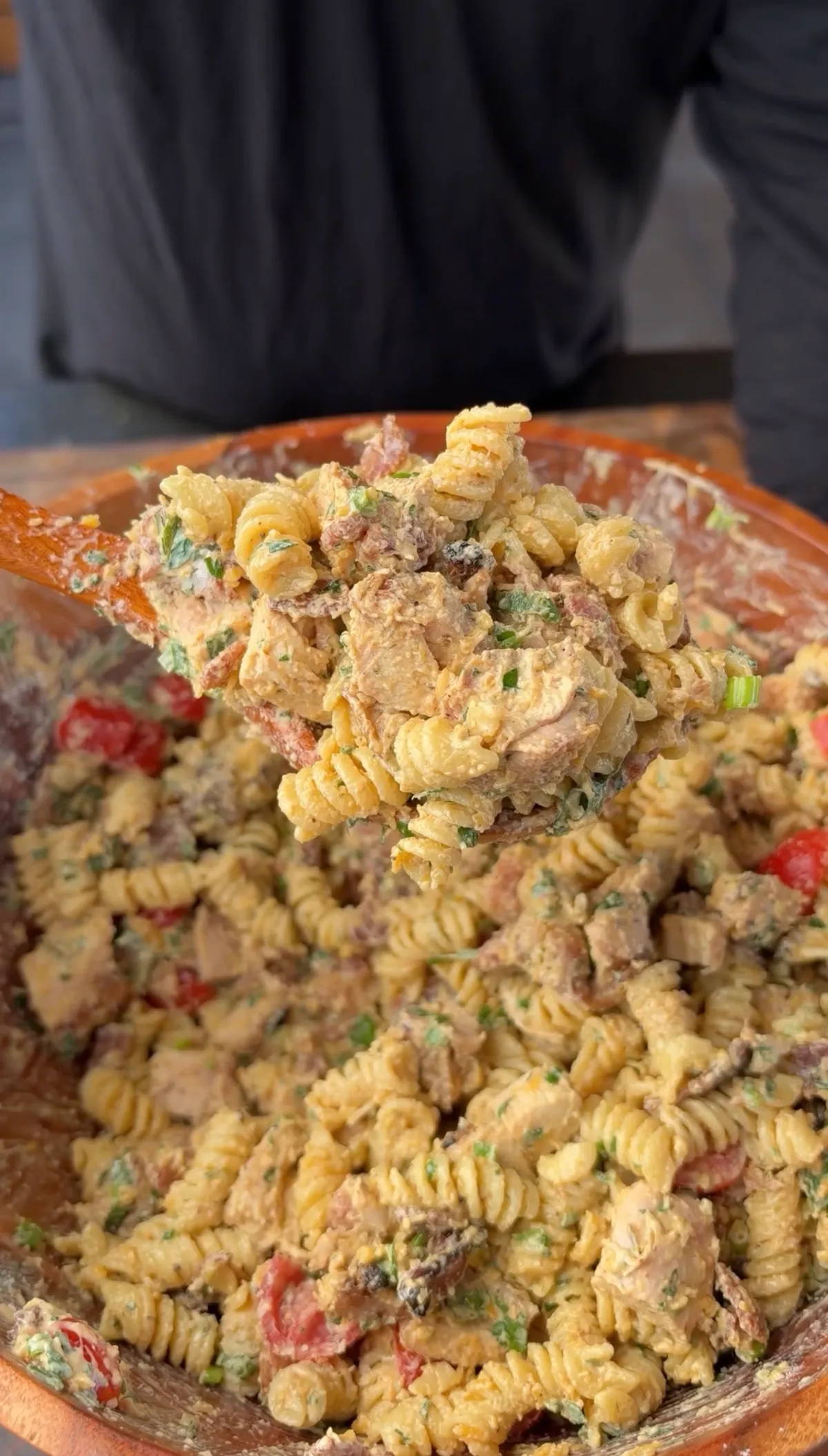 Rotini pasta salad with grilled chicken, crispy bacon, cherry tomatoes, cheddar, and creamy chipotle ranch in a wooden bowl