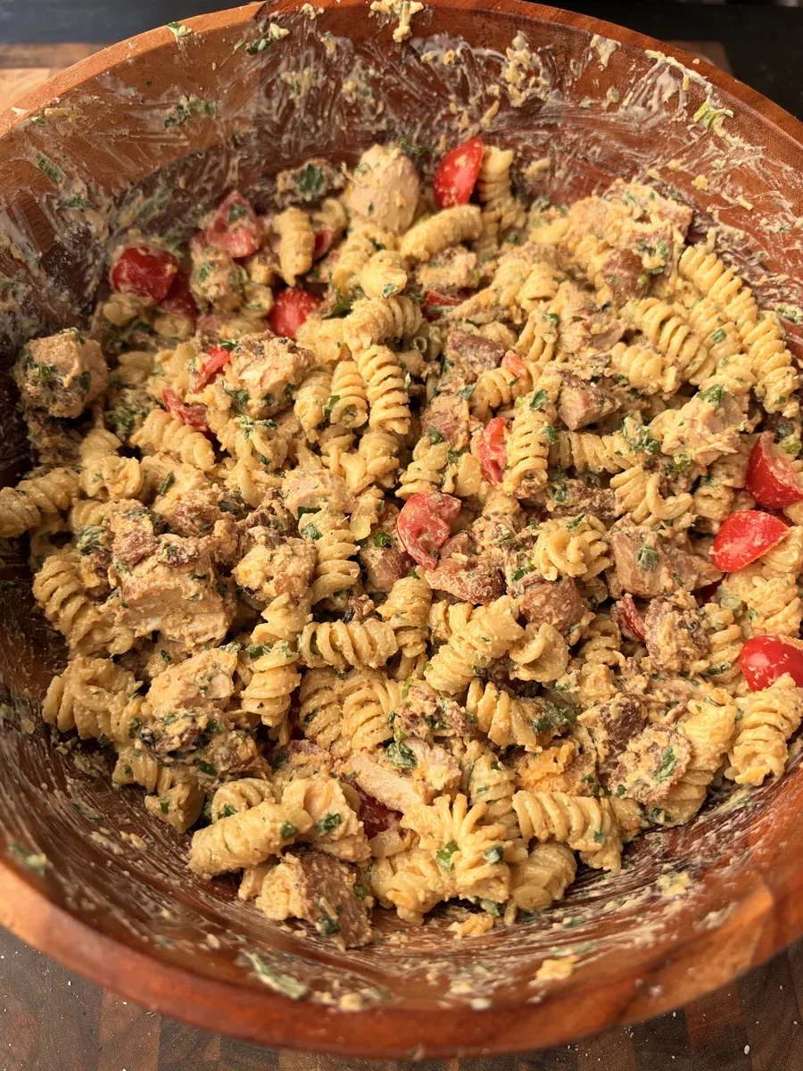 Rotini pasta salad with grilled chicken, crispy bacon, cherry tomatoes, cheddar, and parsley tossed in chipotle ranch in a wooden bowl