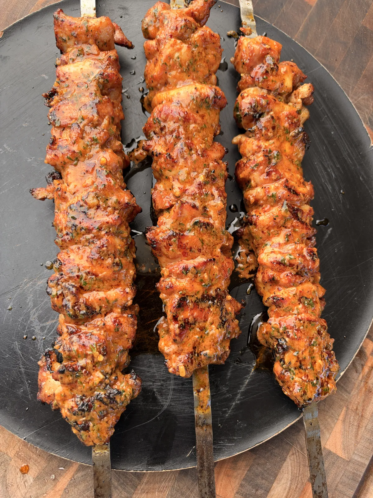 Three grilled chicken thigh skewers basted with cowboy butter, resting on a dark round platter