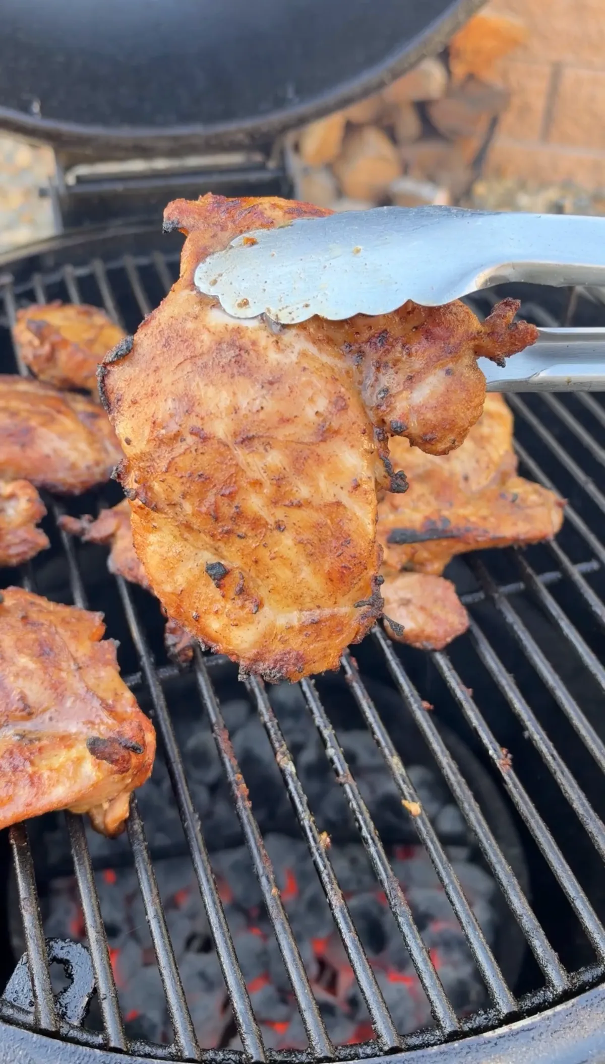 Seasoned boneless skinless chicken thighs grilling over hot charcoal, held with tongs at 185°F