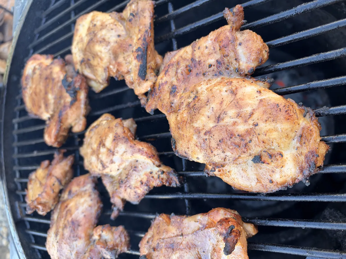 Boneless skinless chicken thighs seasoned with smoked paprika grilling on a charcoal grill until golden brown