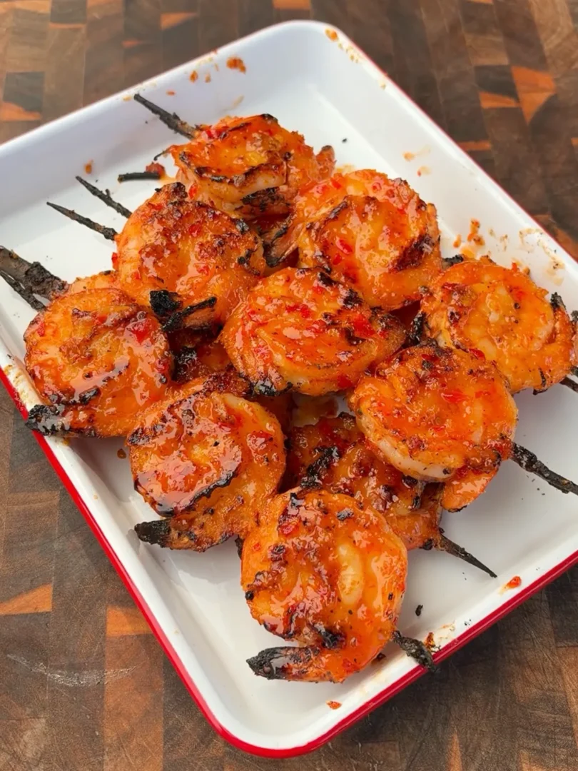 Firecracker glazed grilled shrimp skewers piled on a white enamel tray with sticky sweet chili sriracha glaze